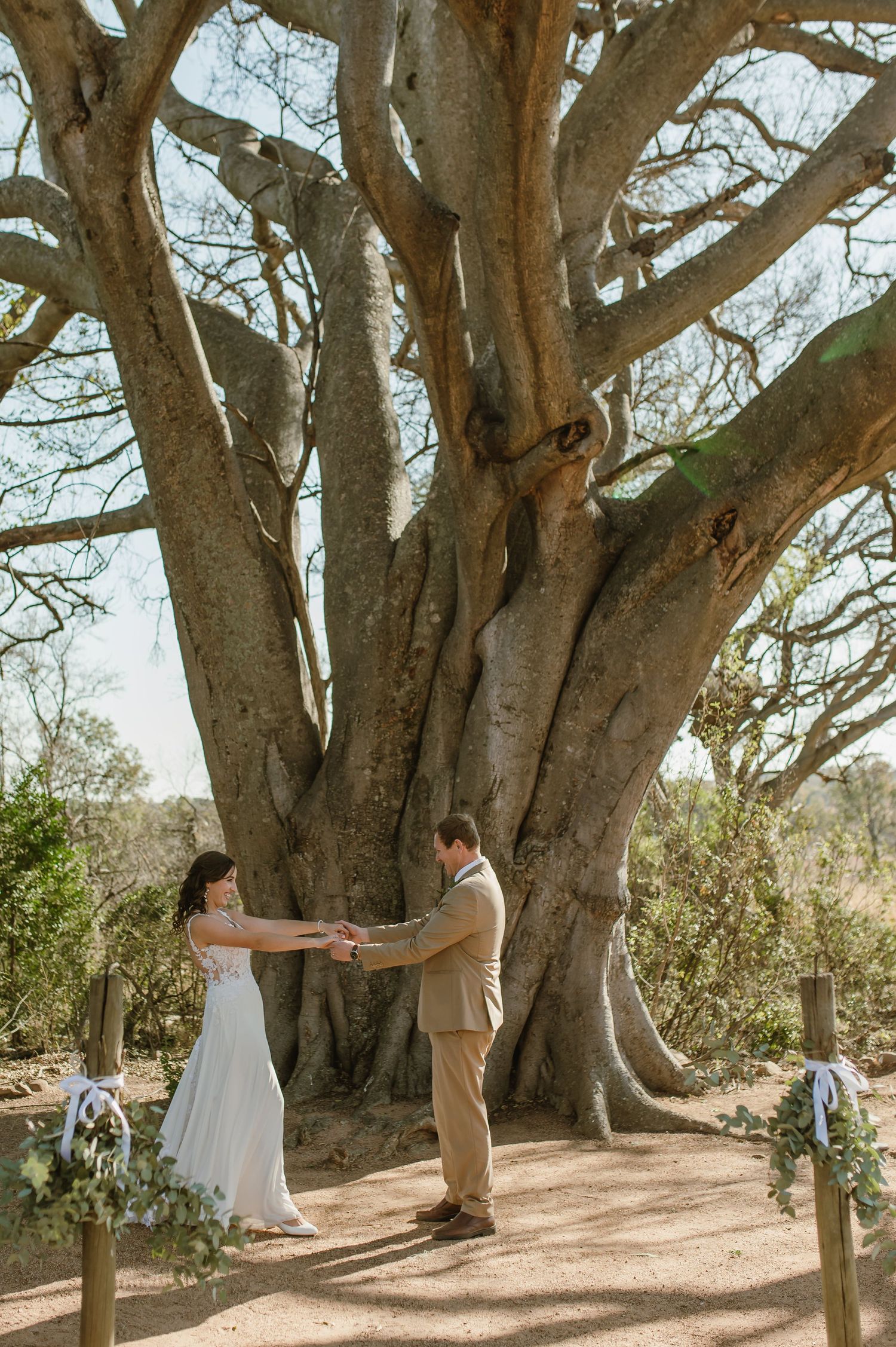 A couple shares intimate moments under majestic trees in a natural outdoor setting.