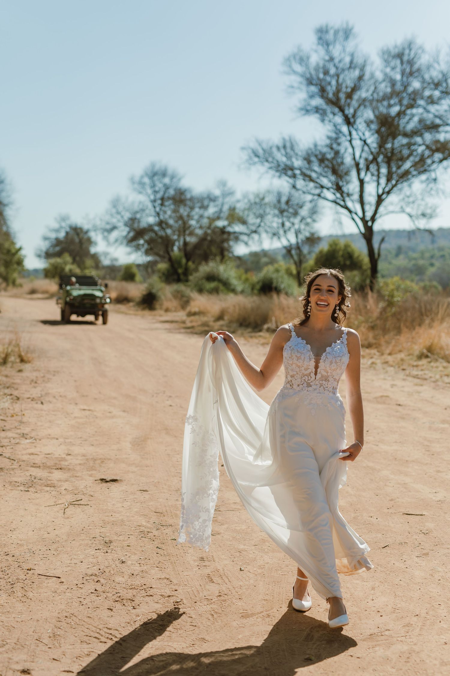Bride dances joyfully in white wedding gown on desert path.