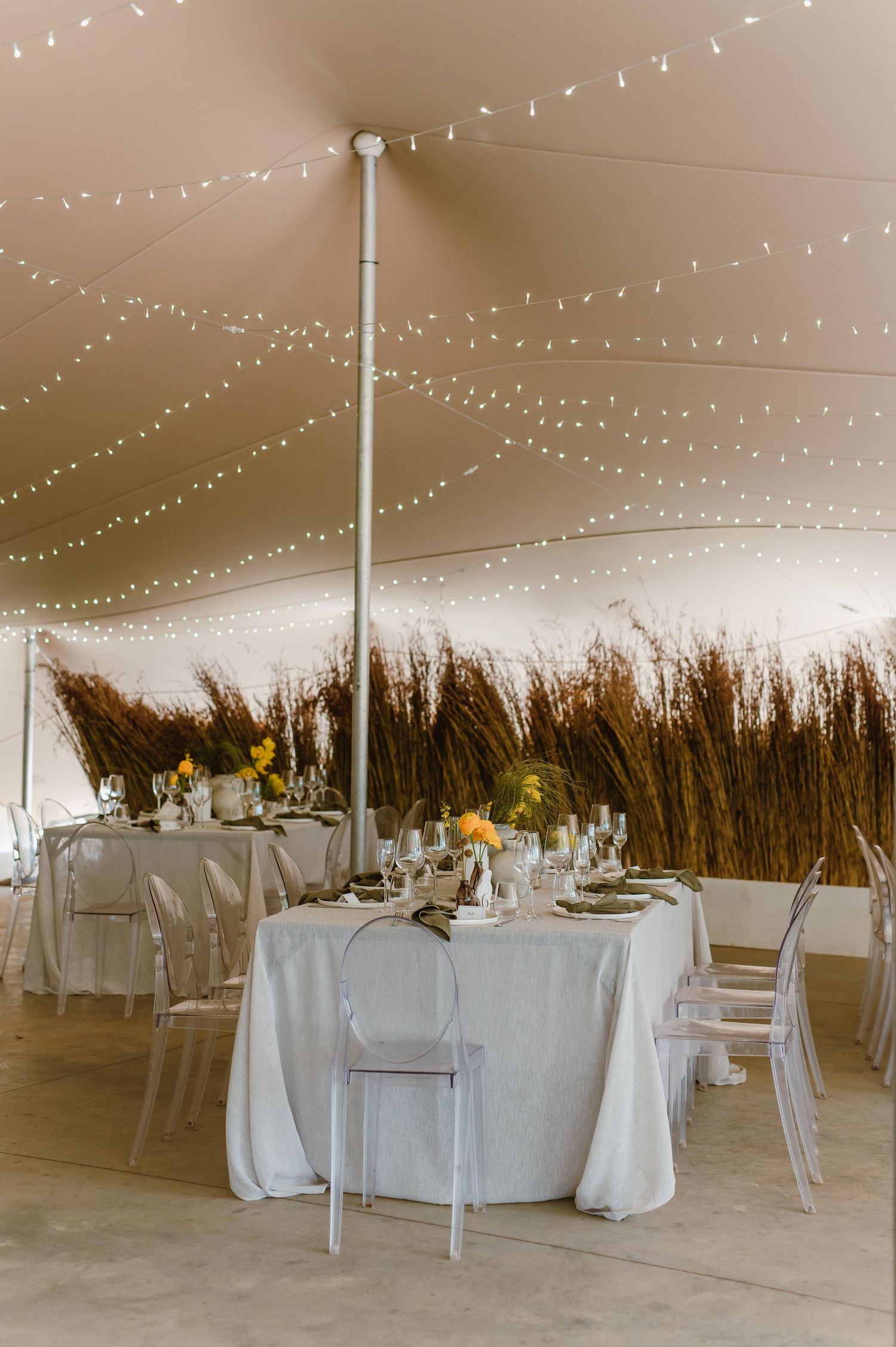 Large white tent reception space with round tables and string light decorations.