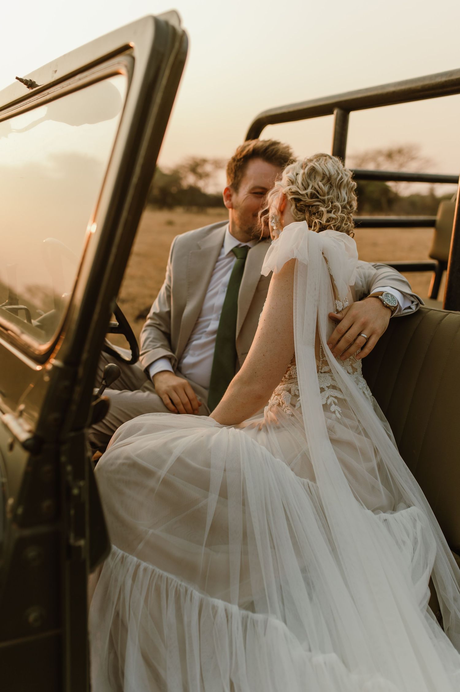 Romantic wedding couple sharing intimate moments inside a vintage vehicle during sunset.