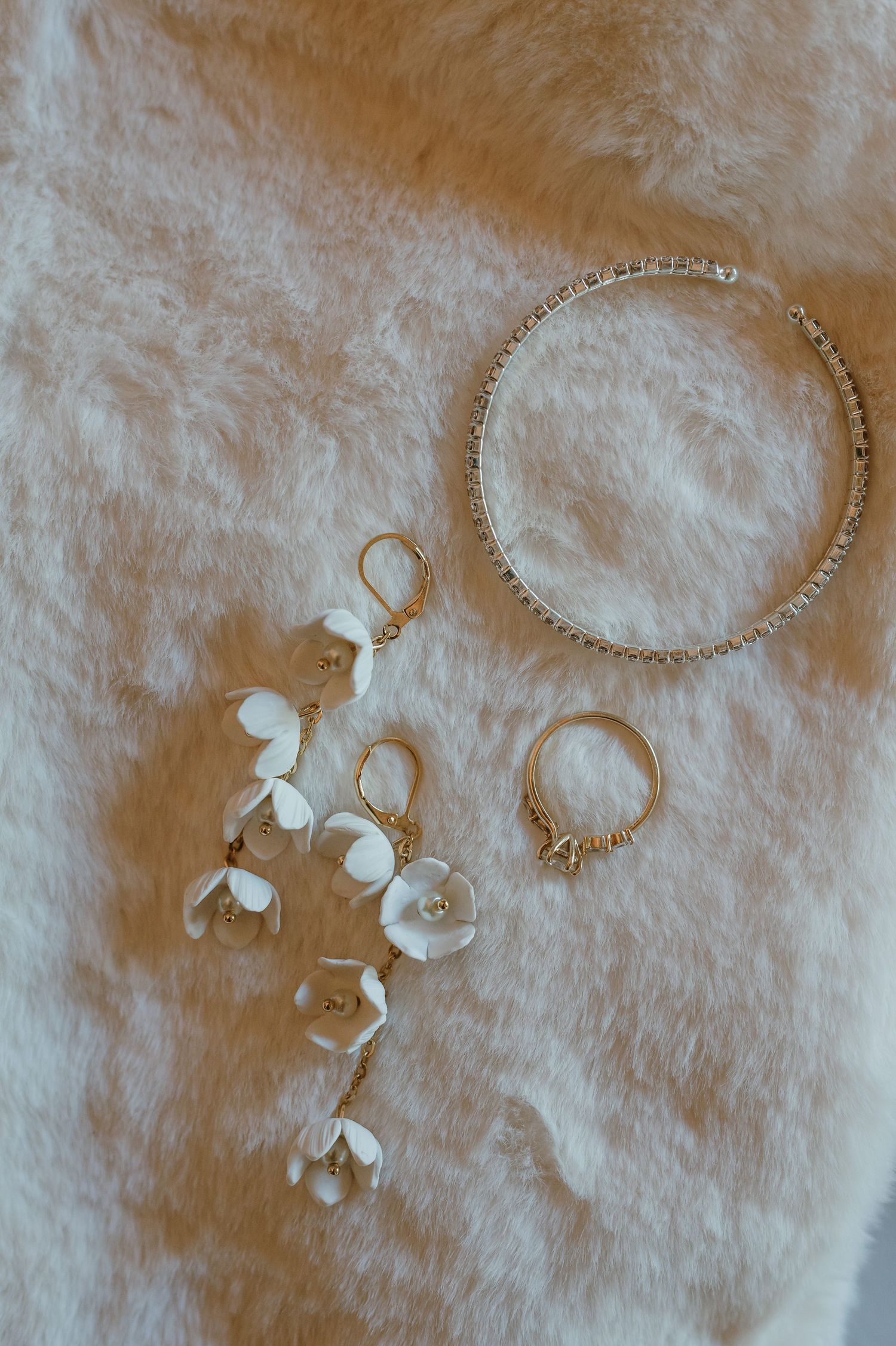 Delicate white floral jewelry and necklace arranged on soft fuzzy fabric.