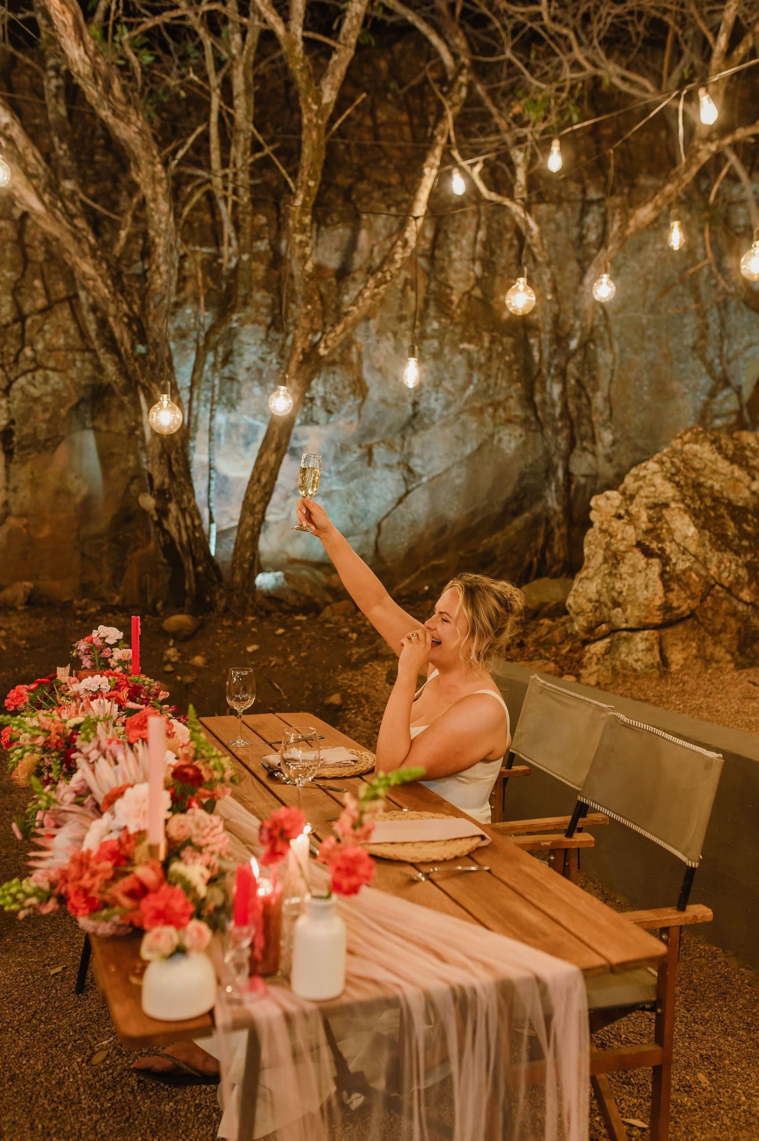 Romantic outdoor dinner setting with string lights and pink floral centerpieces.