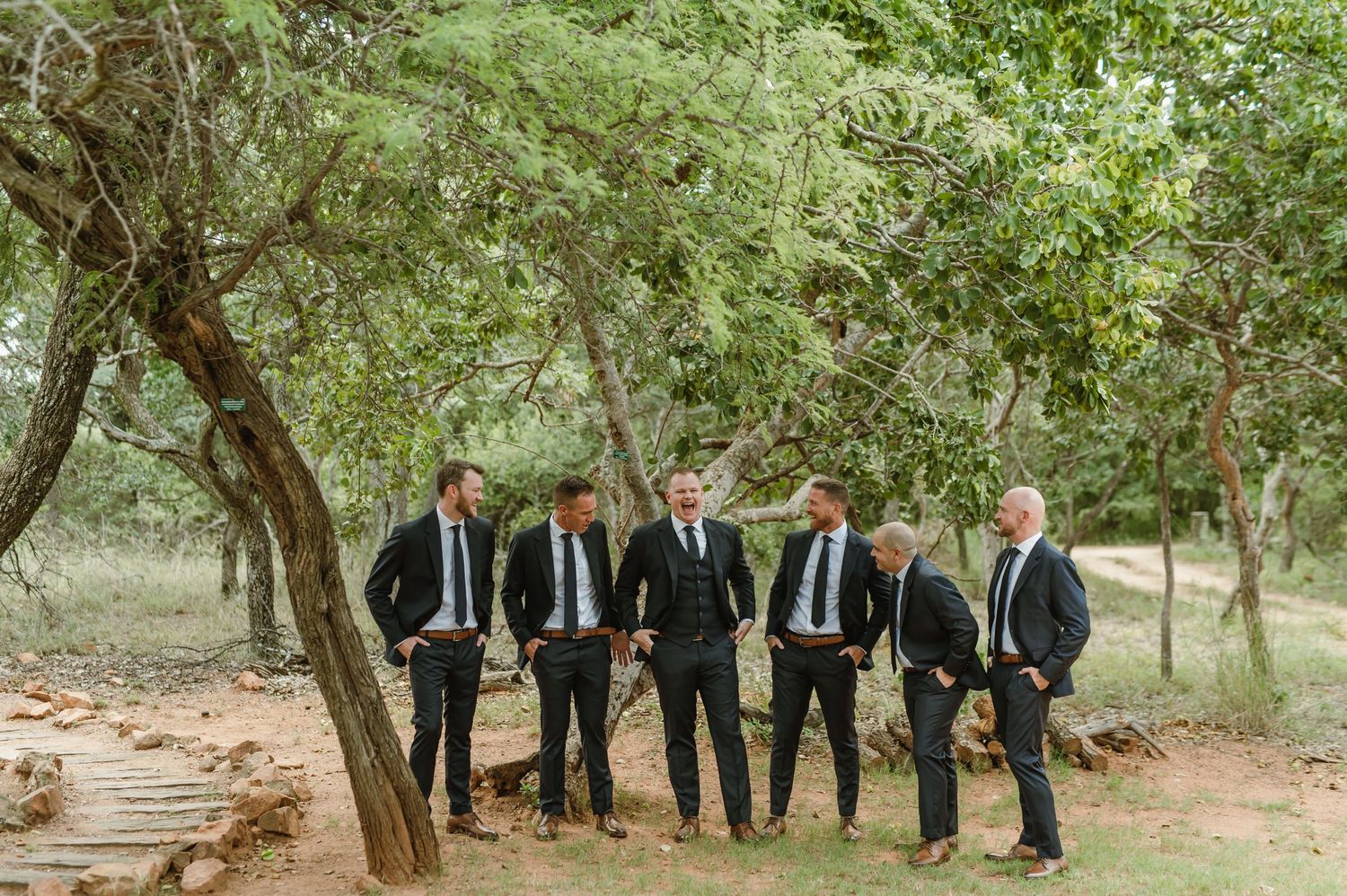 Groomsmen in formal attire standing in a row against a natural wooded backdrop.