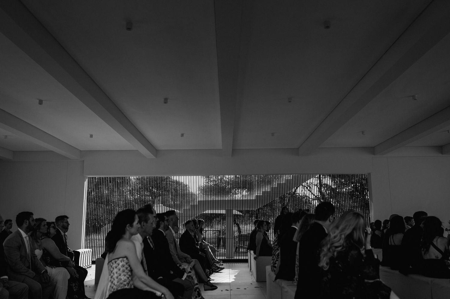 Modern white wedding venue with exposed beams and large windows overlooking nature.