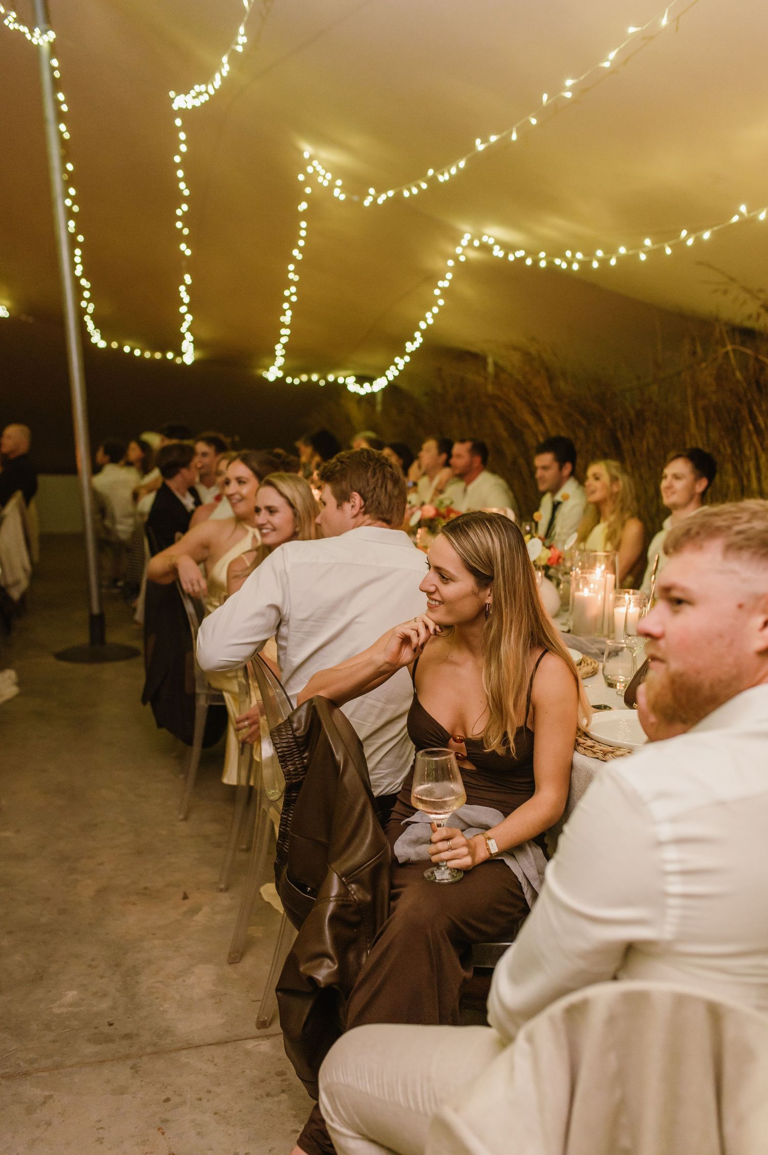Guests enjoying a festive dinner reception under warm string lights in an elegant tent setting.