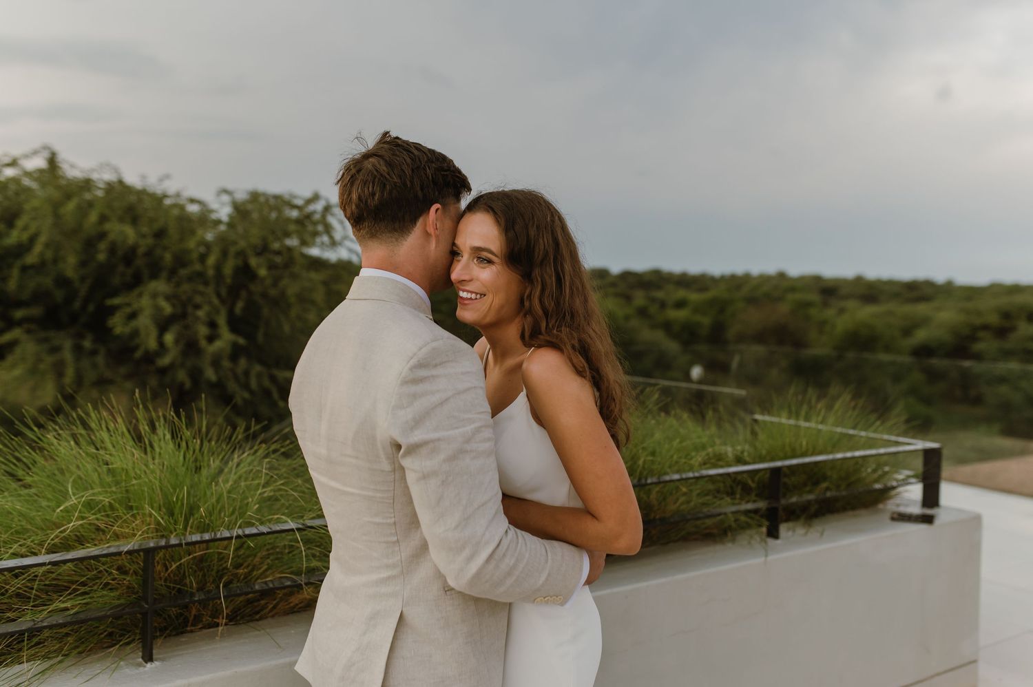Elegant wedding couple poses against scenic waterfront backdrop during sunset photoshoot.