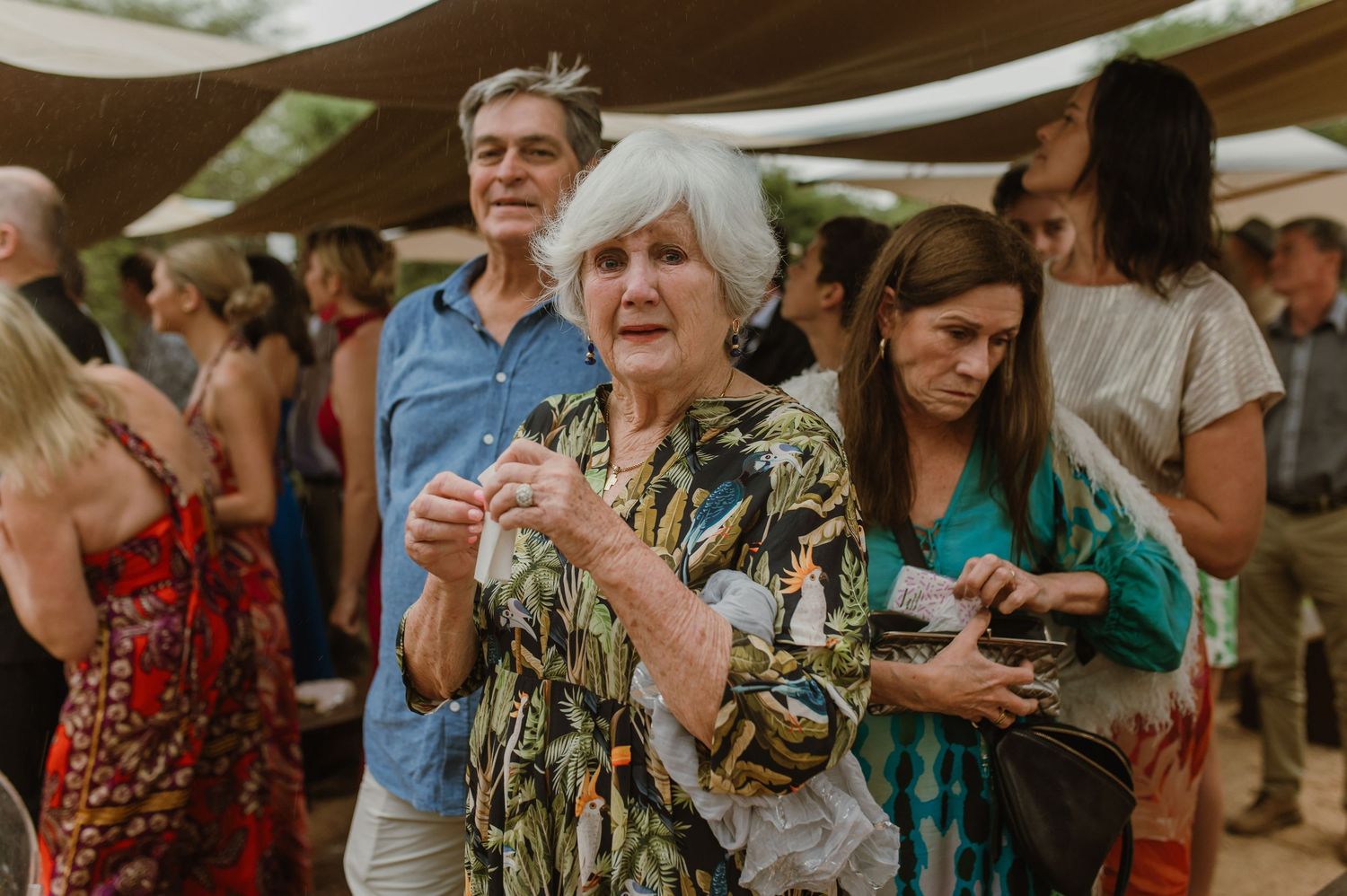 Reception guests in colorful attire socialize at an outdoor wedding venue.