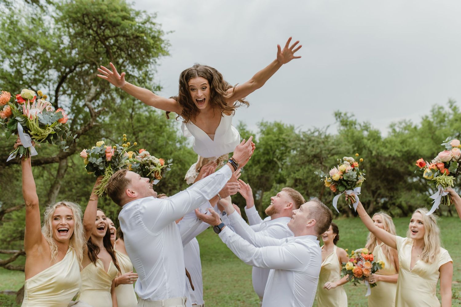 Joyful celebration with bridal party dancing and laughing in an outdoor setting.