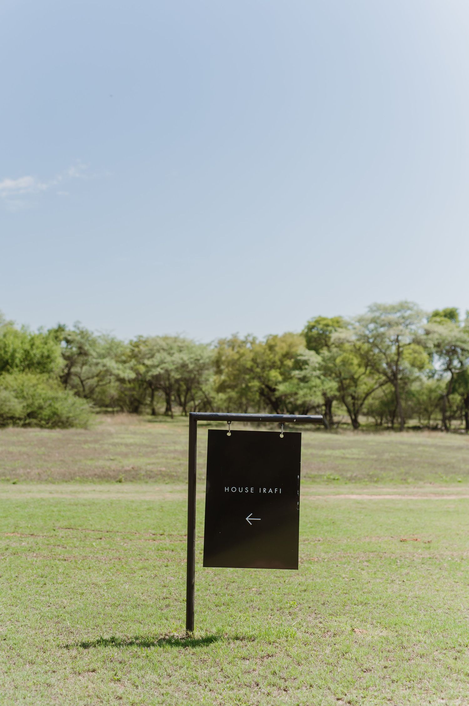 Black directional signs stand in an open grassy field against a blue sky.