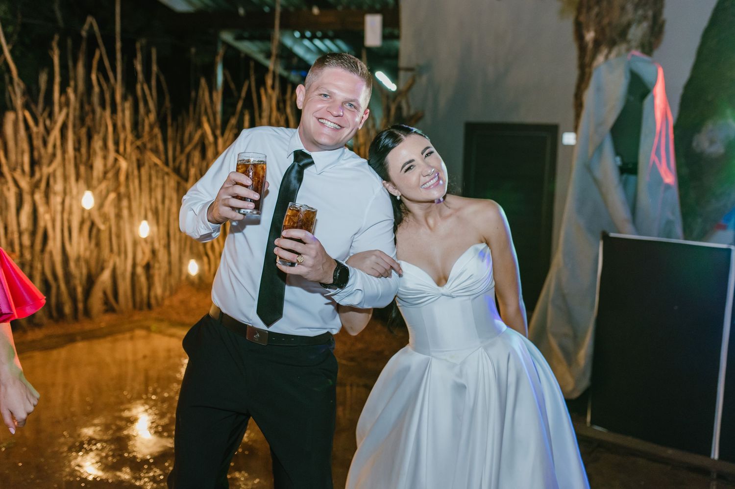 Bride and male guest smiling and holding drinks together at a festive wedding reception.