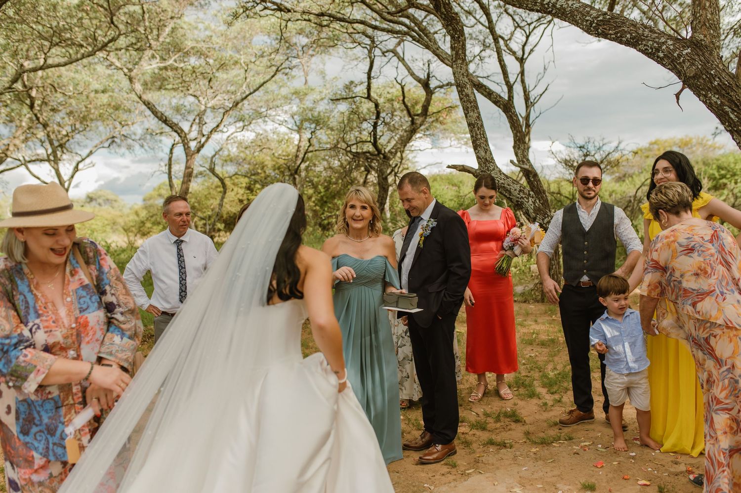 Bride in white gown and veil walking toward smiling groom surrounded by wedding guests.