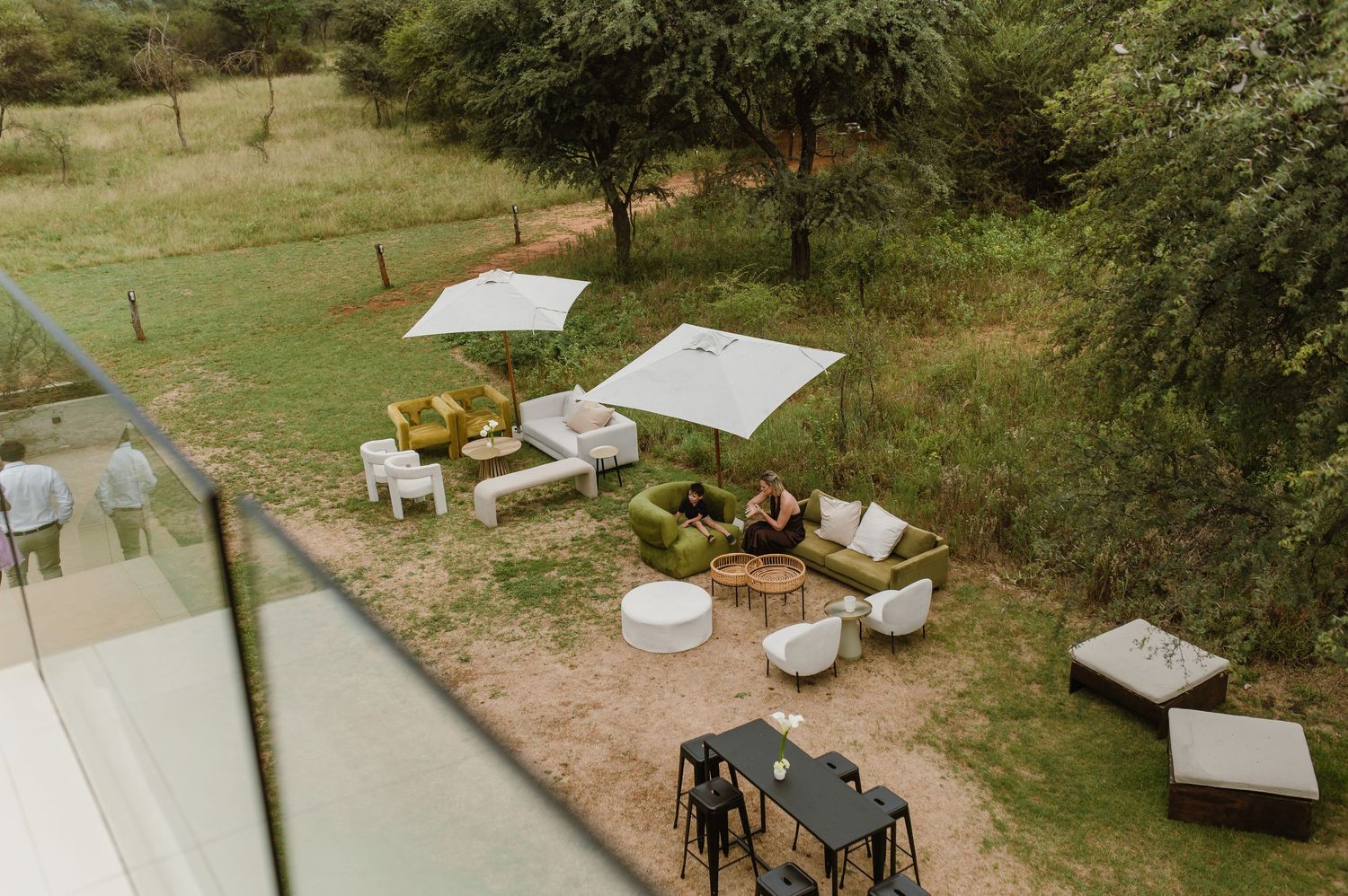 Aerial view of outdoor lounge setup with white furniture and umbrellas in a garden setting.