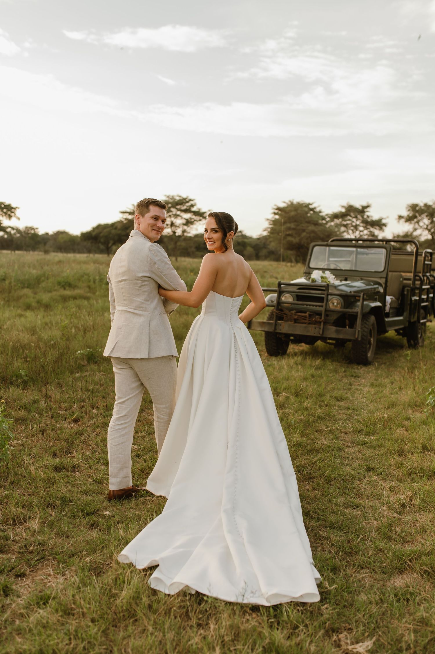 A romantic wedding couple dances together in a grassy field at sunset with a vintage truck in the background.