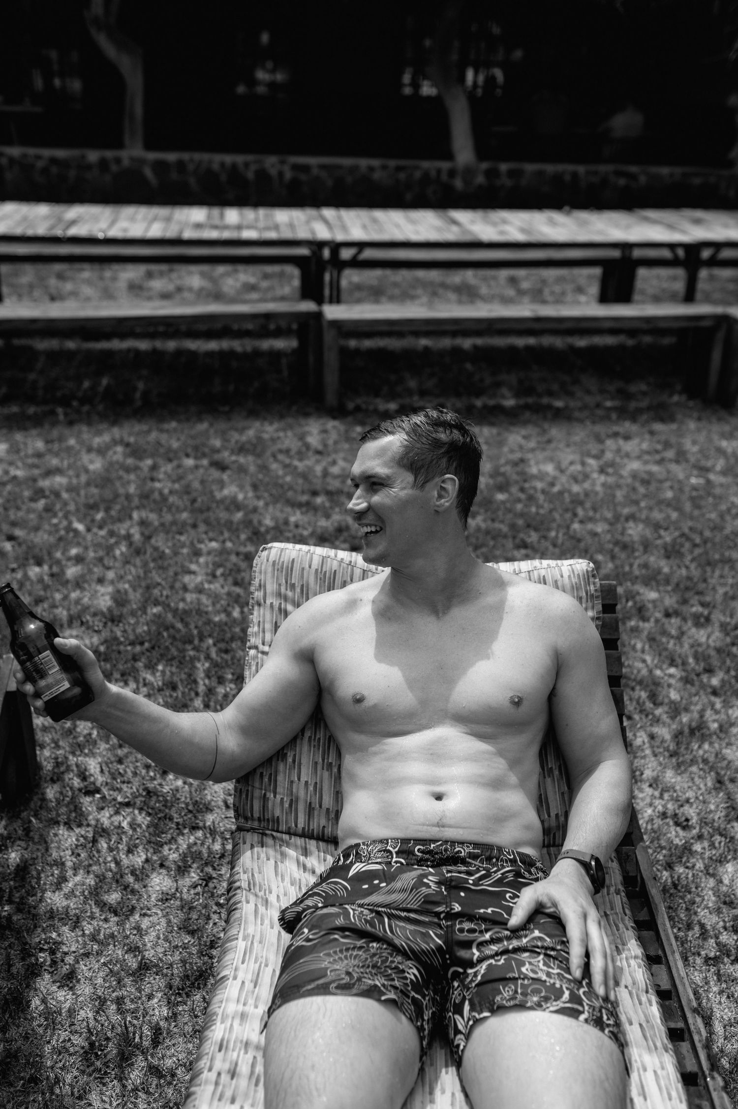Two people relaxing on lounge chairs outdoors wearing patterned shorts and enjoying beverages.
