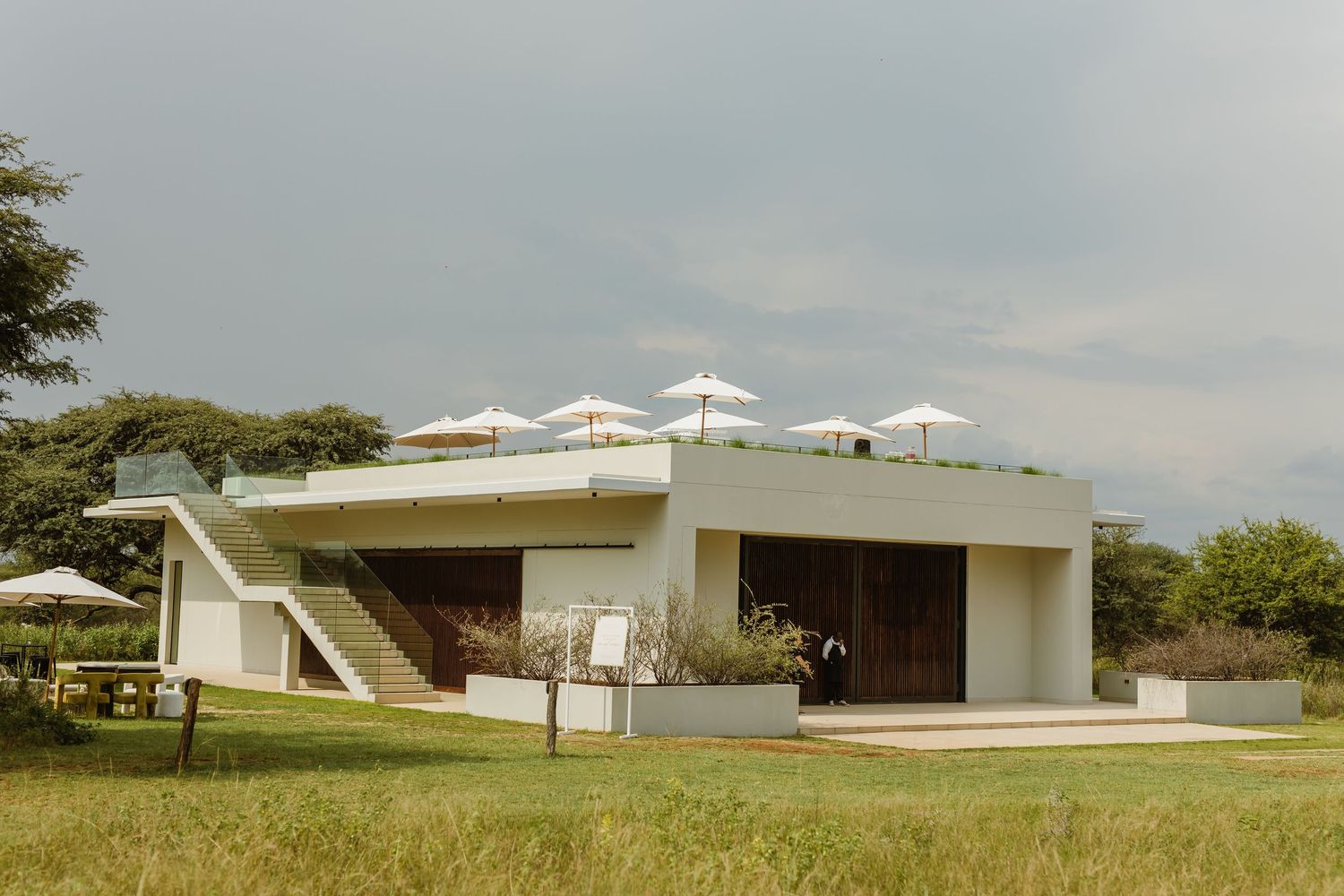 Modern white wedding venue buildings with geometric architecture set against a grassy landscape and cloudy sky.