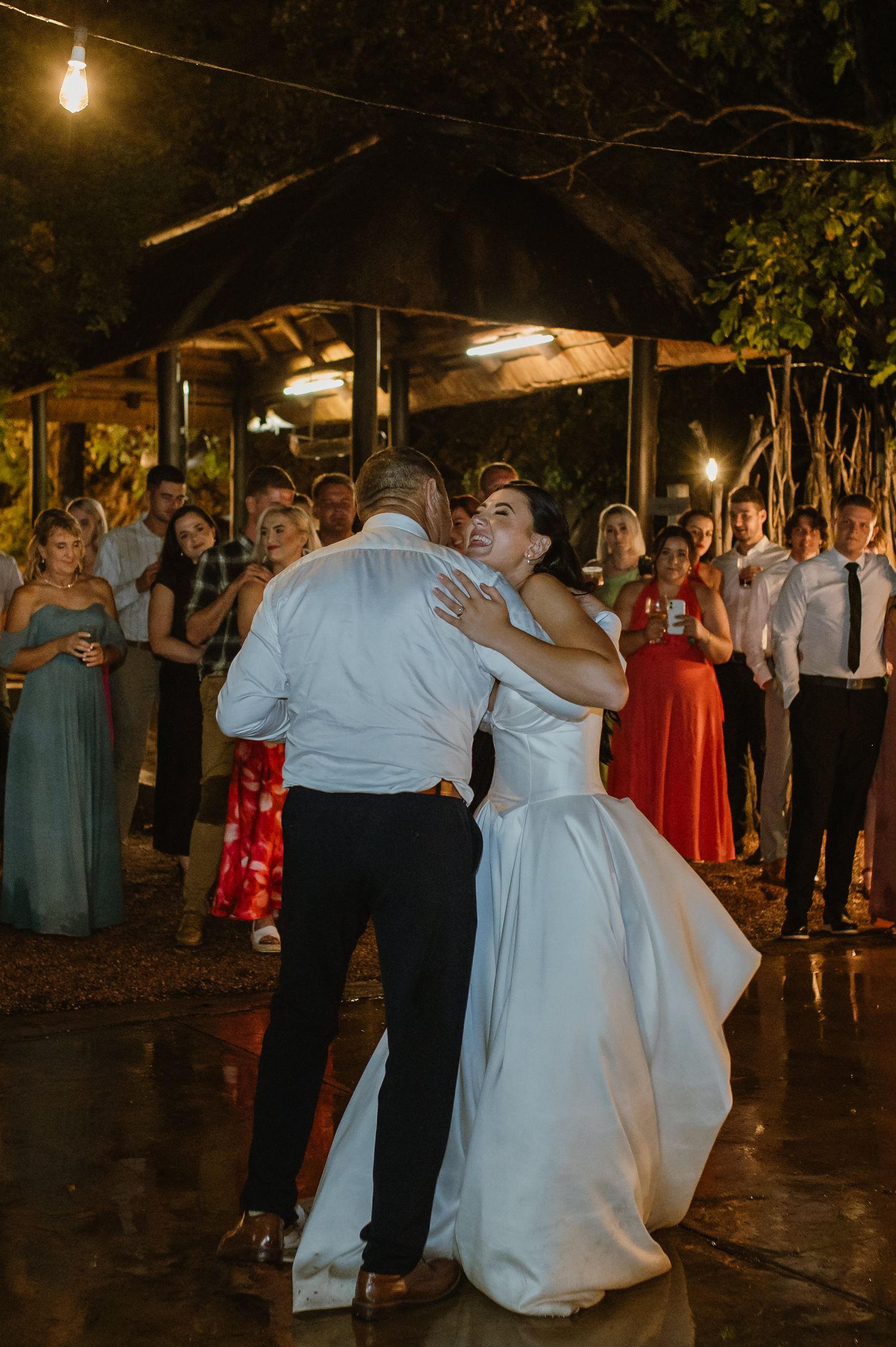 Bride shares emotional father-daughter dance under string lights at outdoor evening wedding reception.