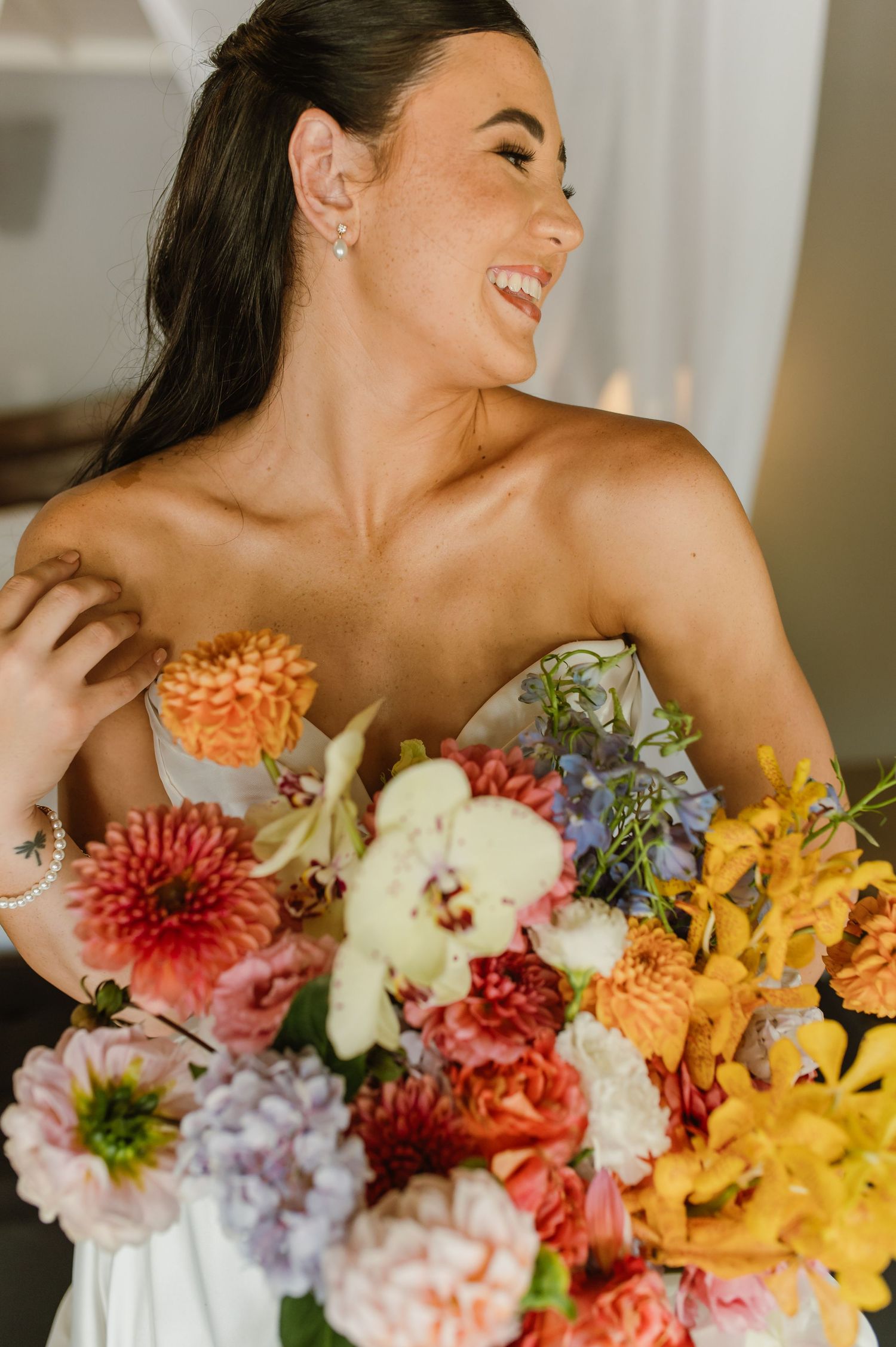 Radiant bride laughing while holding colorful bouquet of dahlias and mixed flowers in white gown.