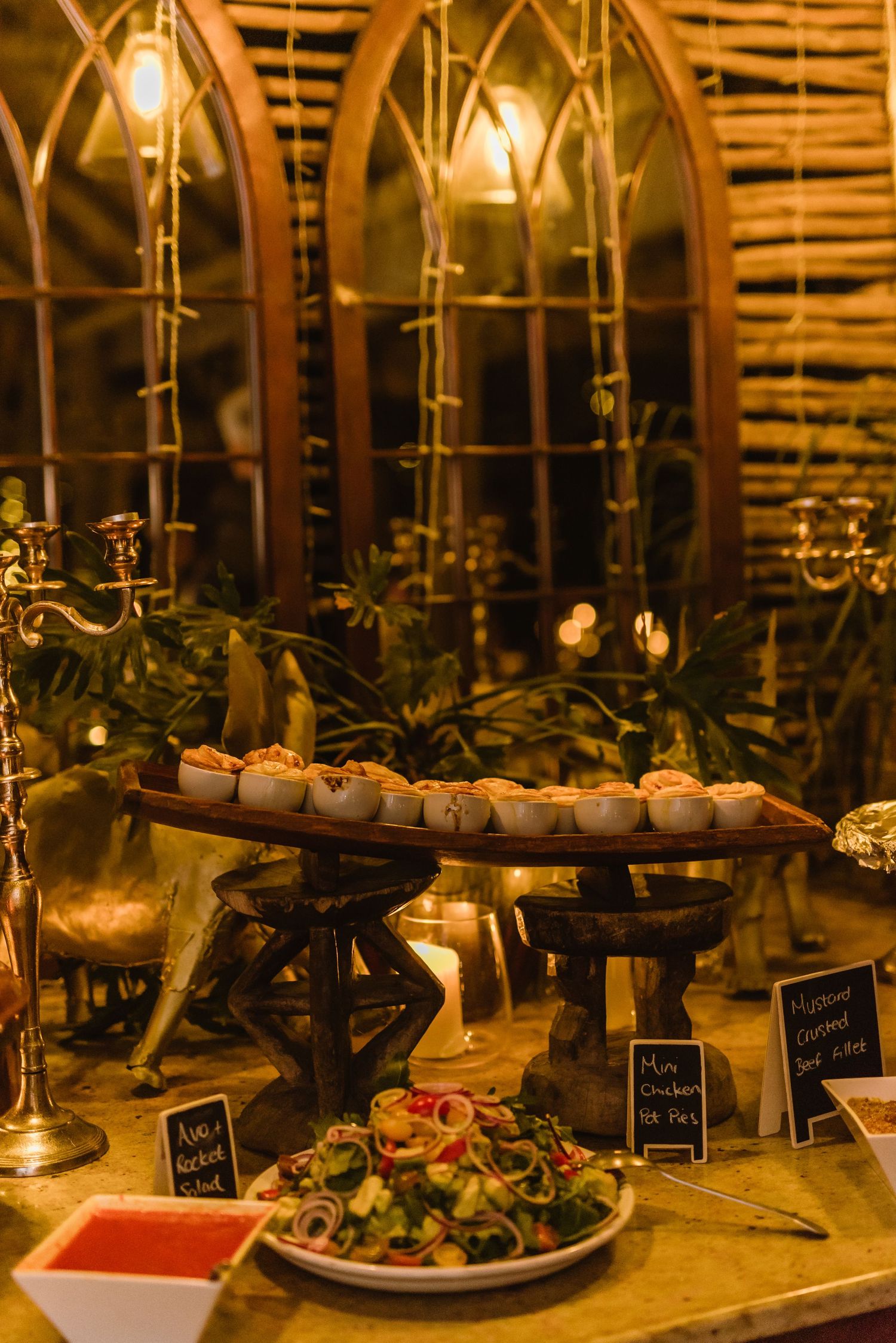 Buffet table with appetizers and small plates illuminated by candlelight at an evening event.