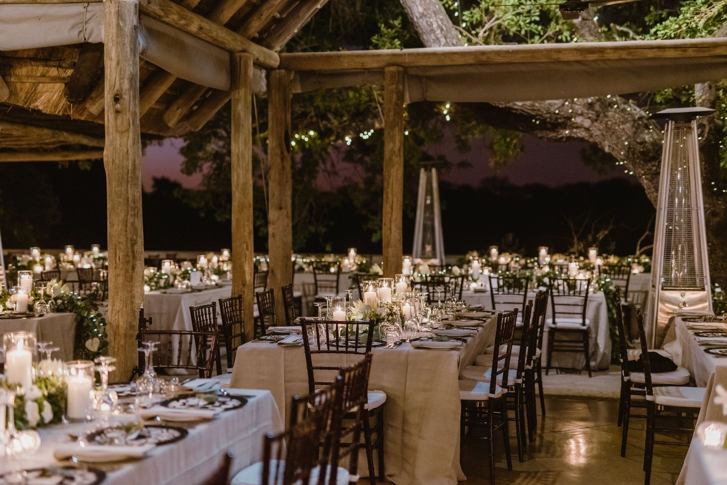 Wedding reception tables arranged under rustic wooden beams with ambient lighting and elegant decor.