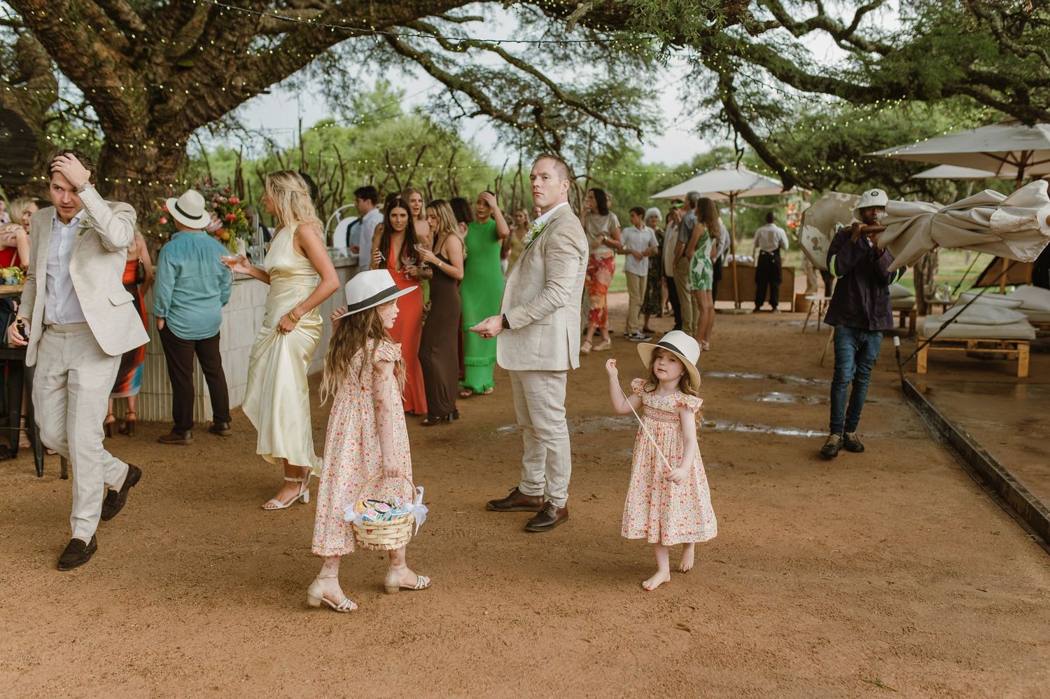 Wedding guests mingling on a dirt path under trees at an outdoor venue.