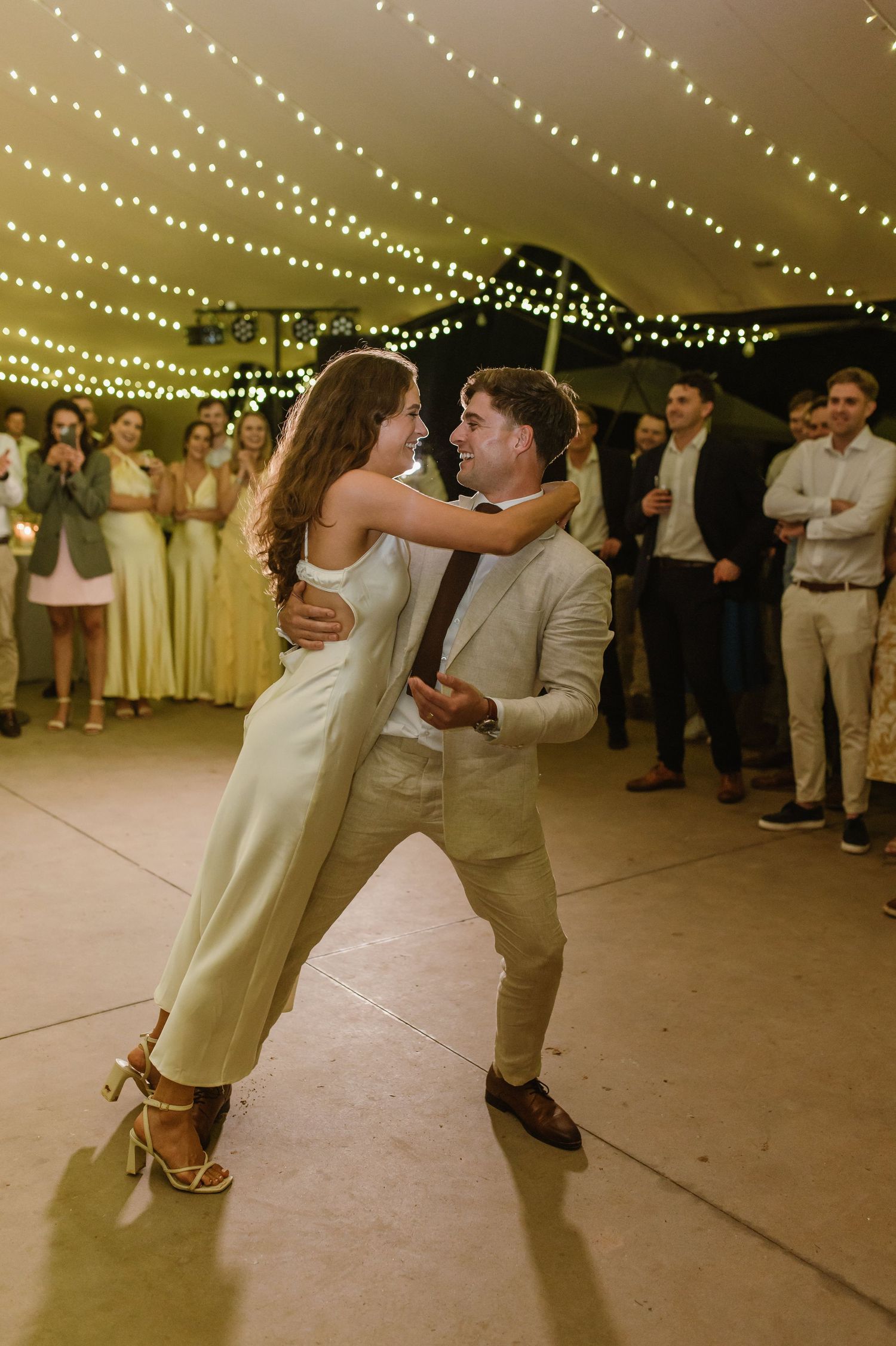 Wedding dancers execute an elegant dance move on the reception floor beneath string lights.