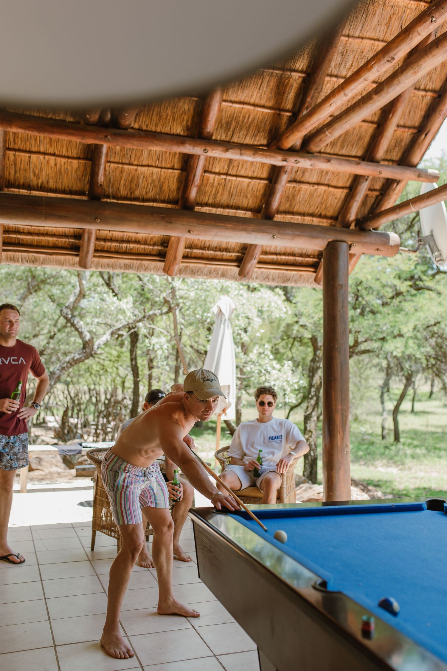 Group enjoying a casual pool game in an open-air thatched pavilion.
