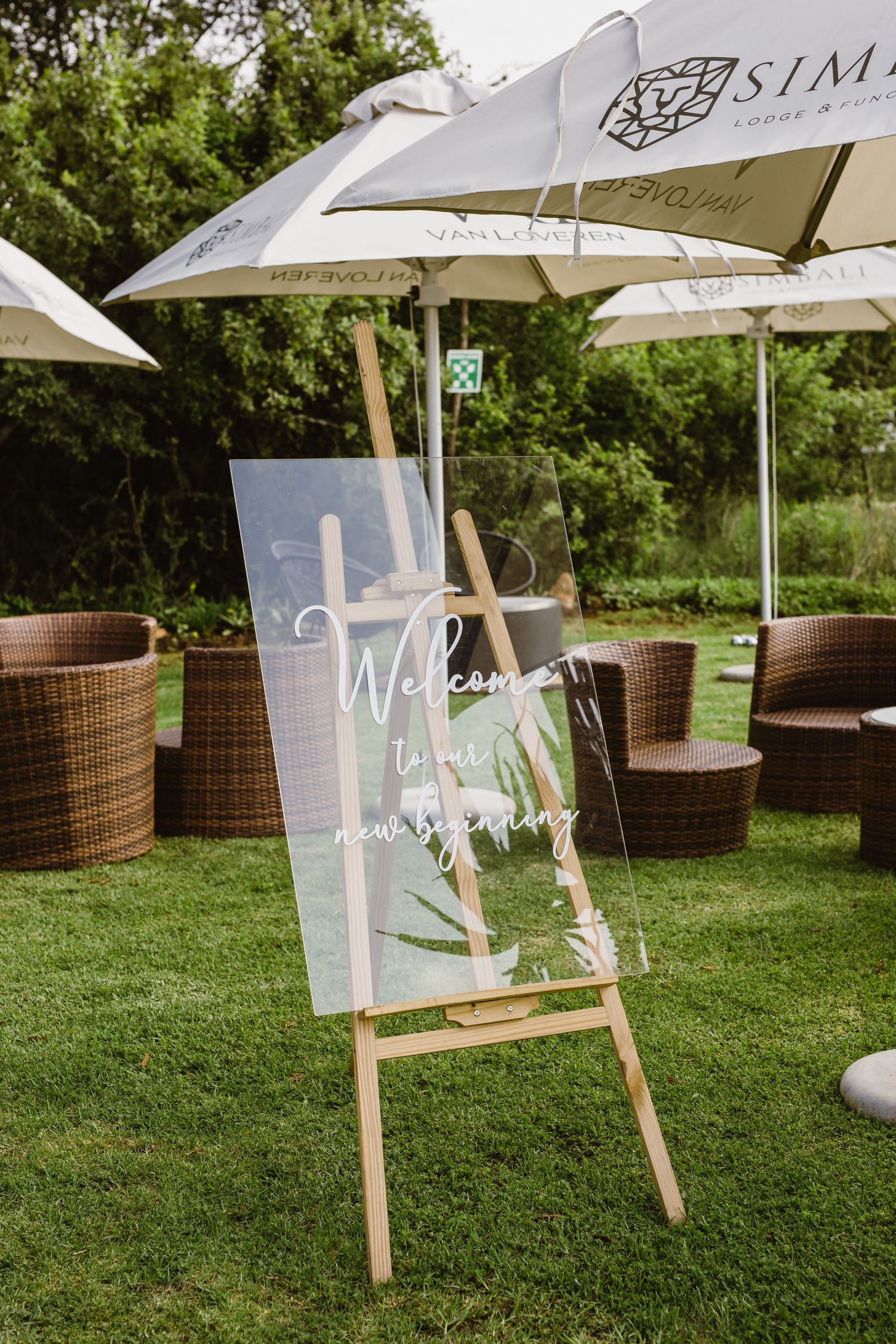 Wedding welcome signs displayed on easels under white umbrellas on grass.
