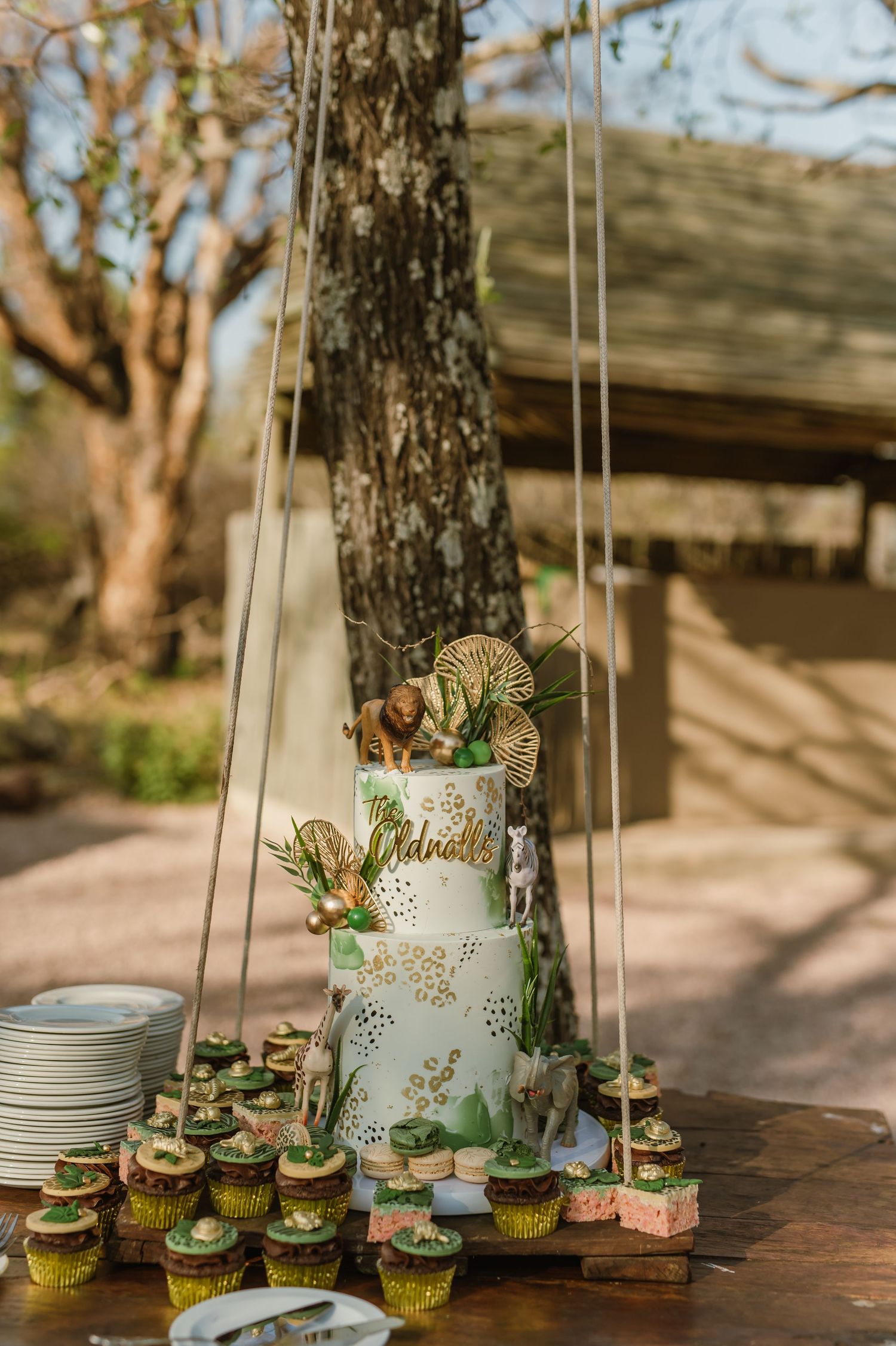Elegant white wedding cake with greenery displayed on rustic wooden table outdoors.
