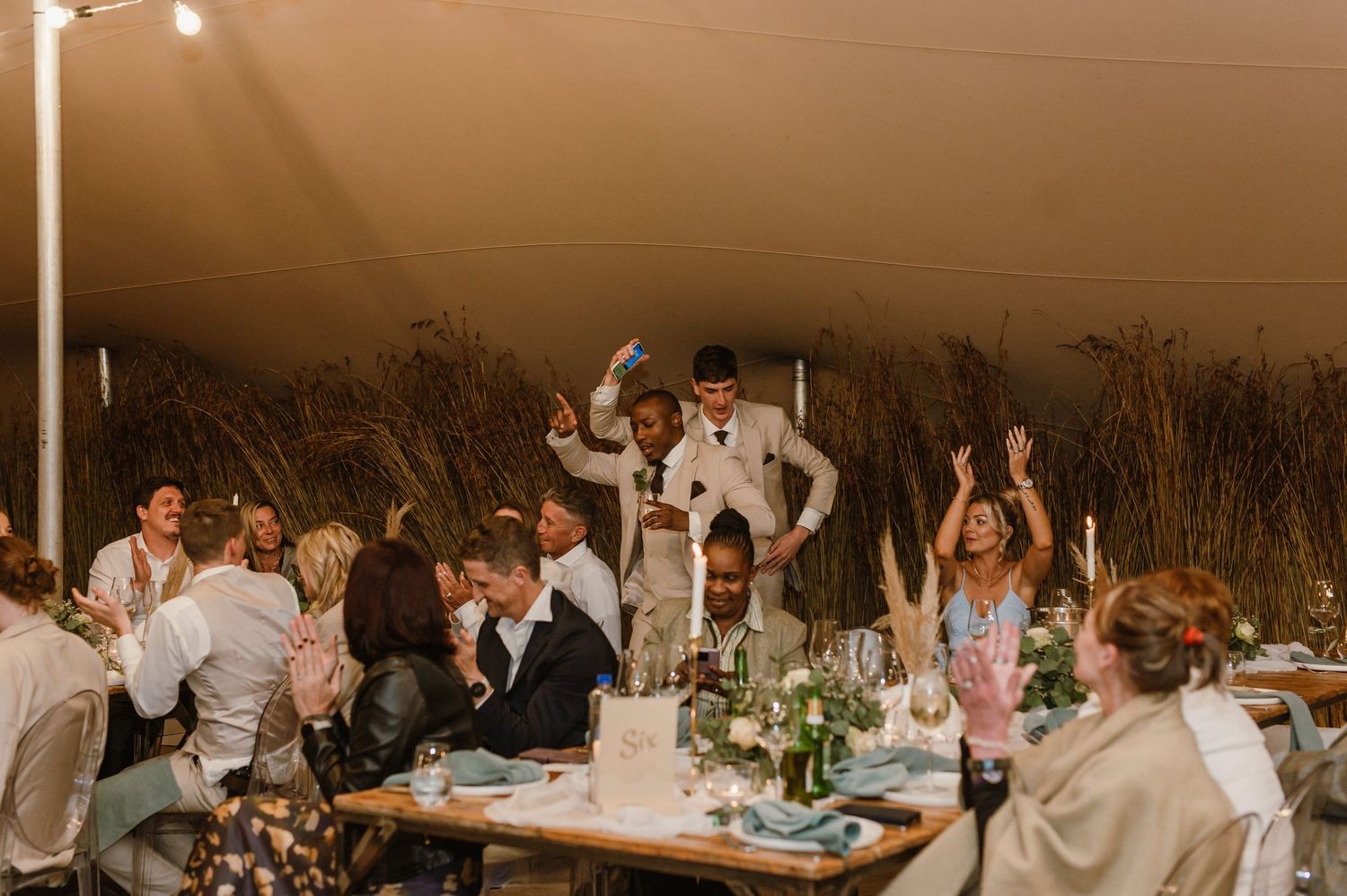 Wedding guests celebrating and dancing under tent with string lights at night.