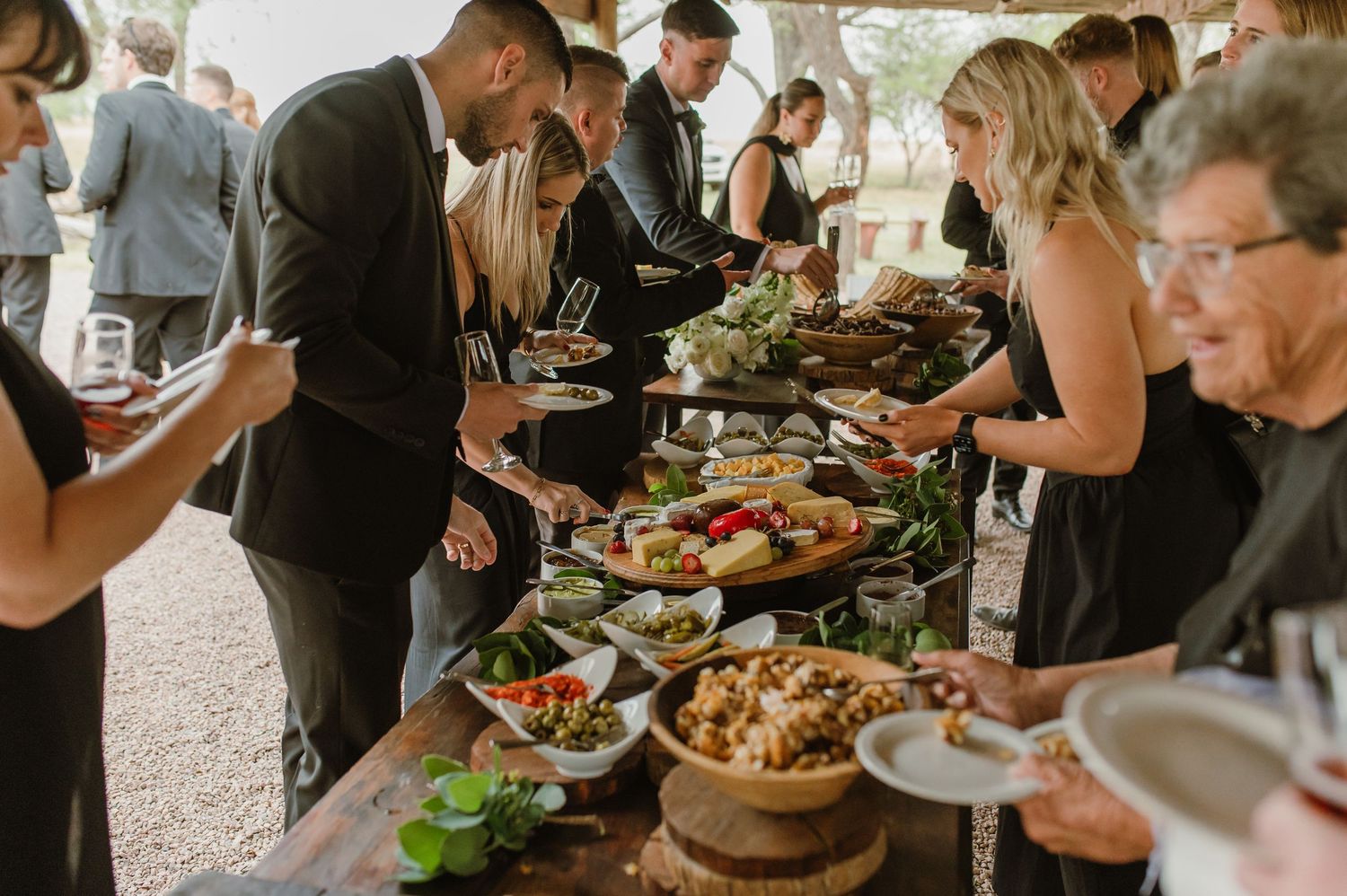 Wedding guests serving themselves at buffet table filled with fresh salads and appetizers.