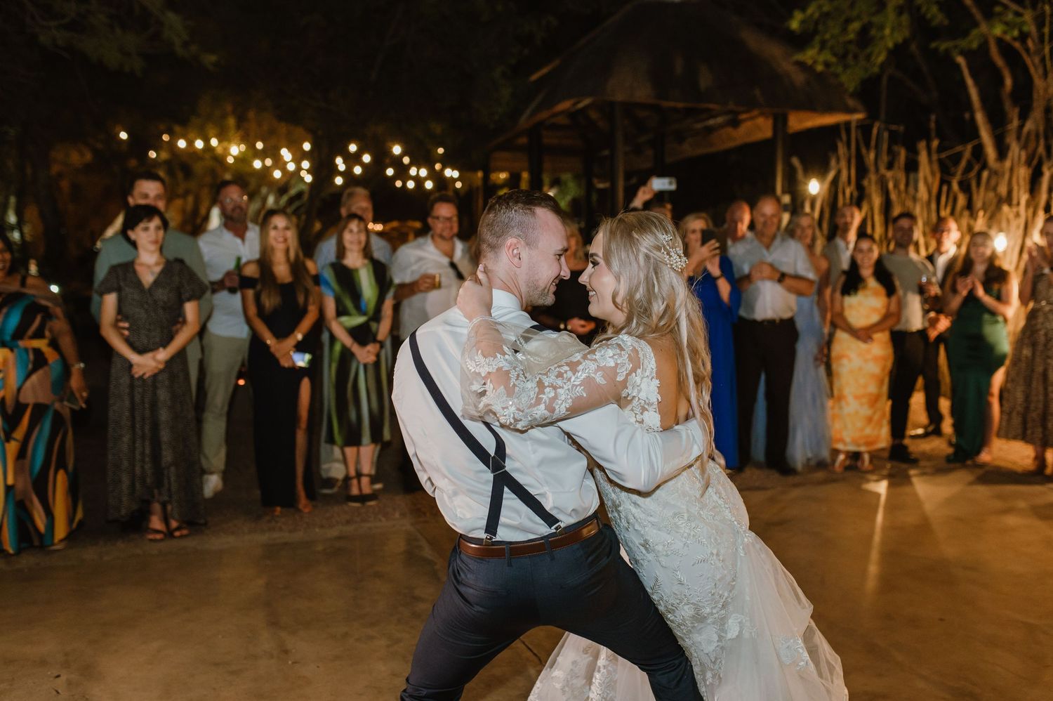 A couple performs a dramatic dip during their wedding dance under twinkling lights outdoors.