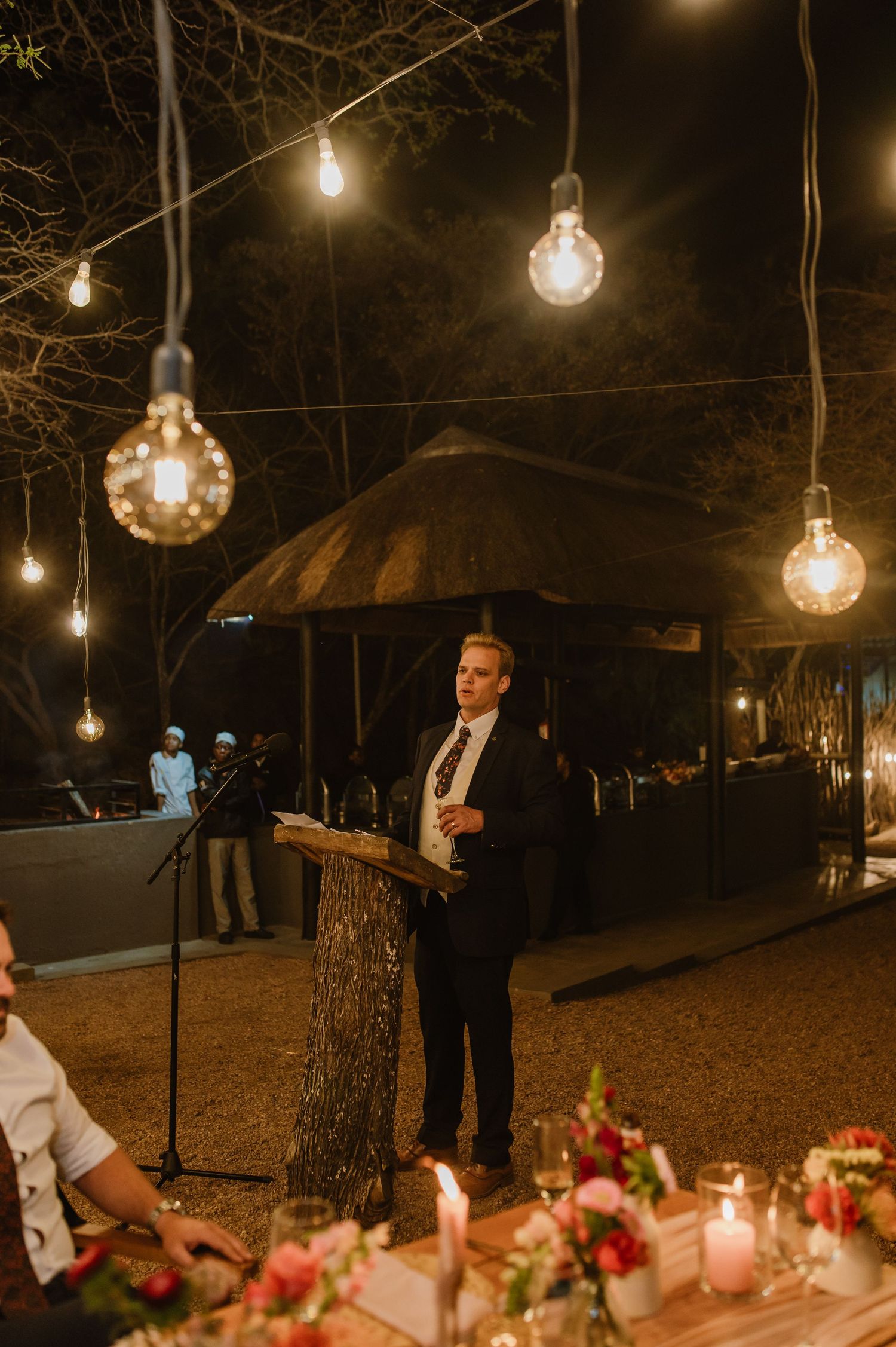 Evening outdoor celebration with hanging globe lights illuminating the trees and dining area.
