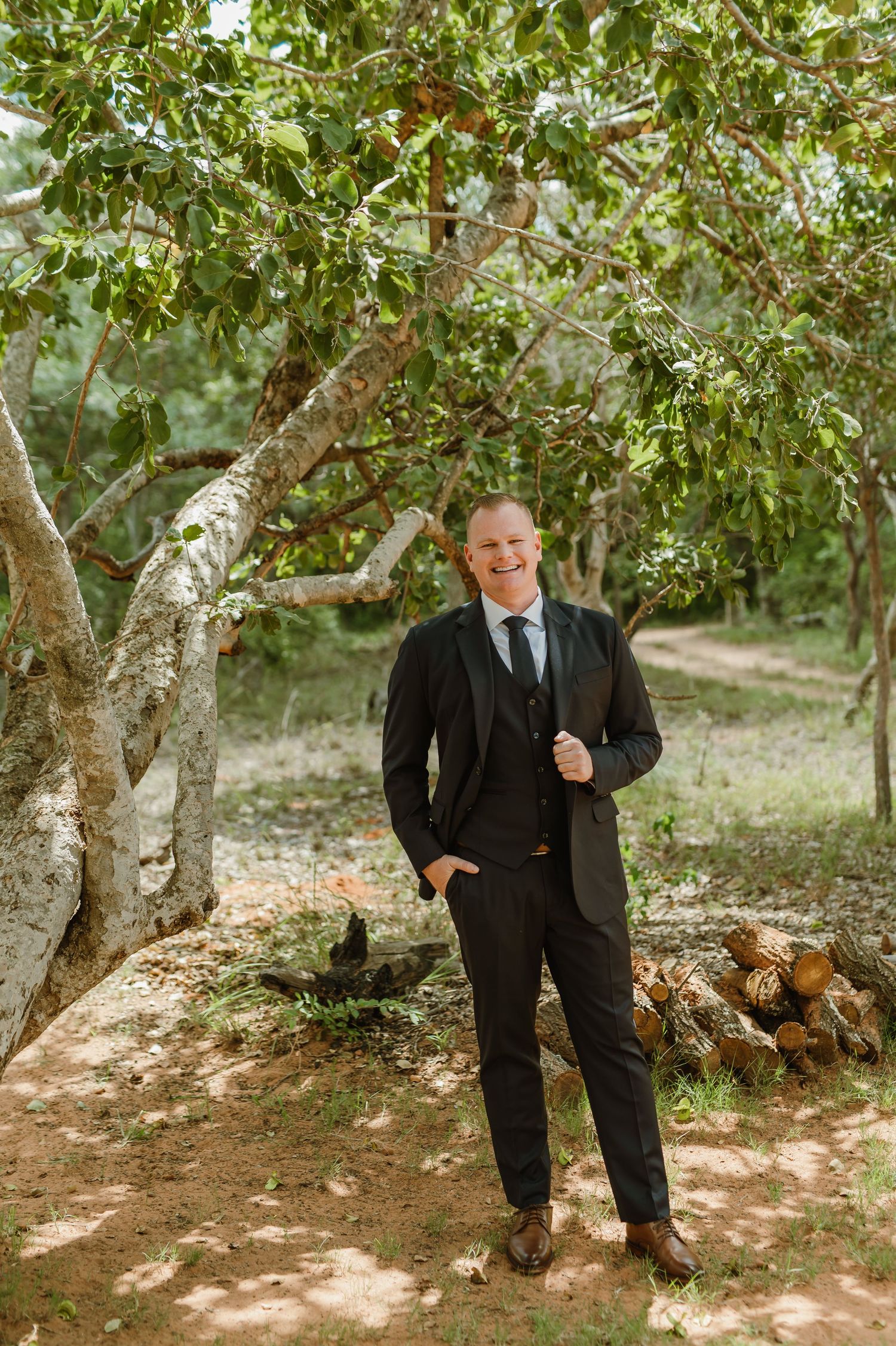 Men in black suits posing under green trees in an orchard setting.