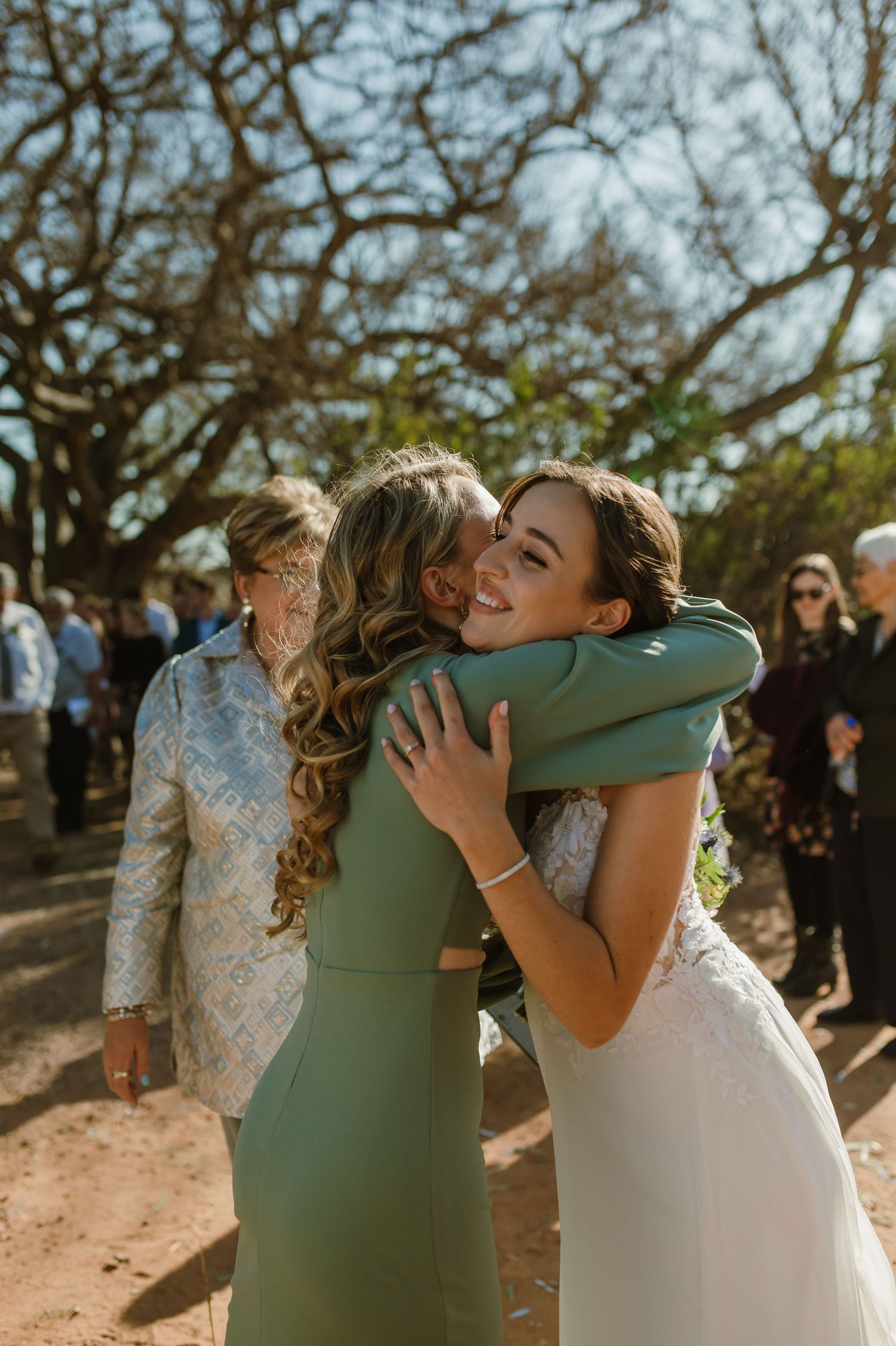 Emotional wedding moment captured in warm sunlight under ancient trees.