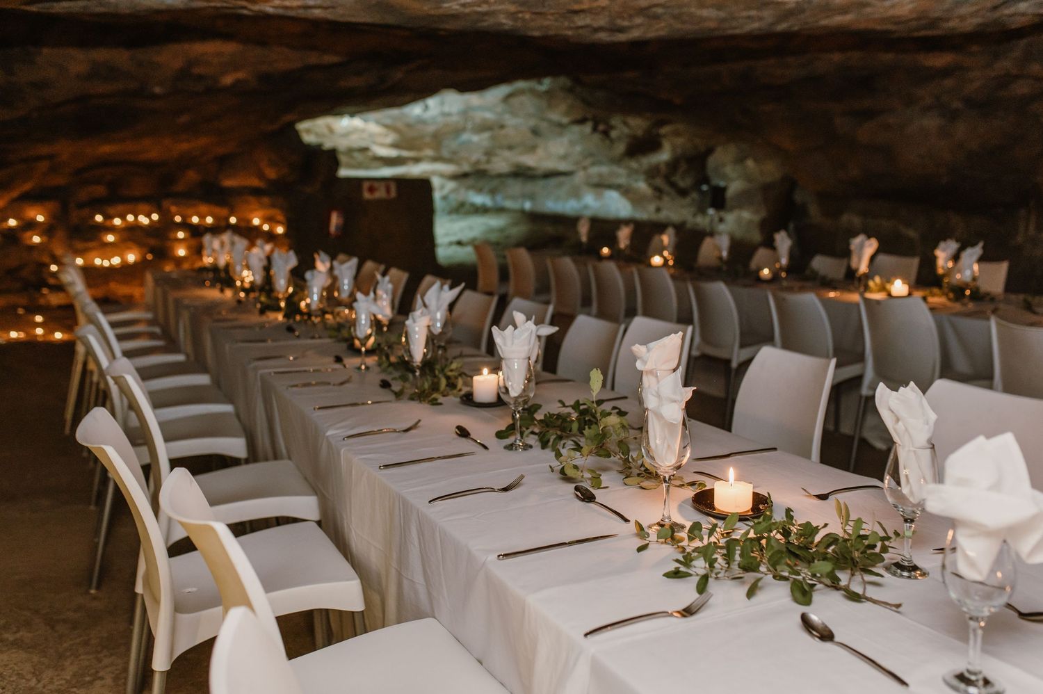 Elegant white table settings arranged in a cave for a formal dining event.