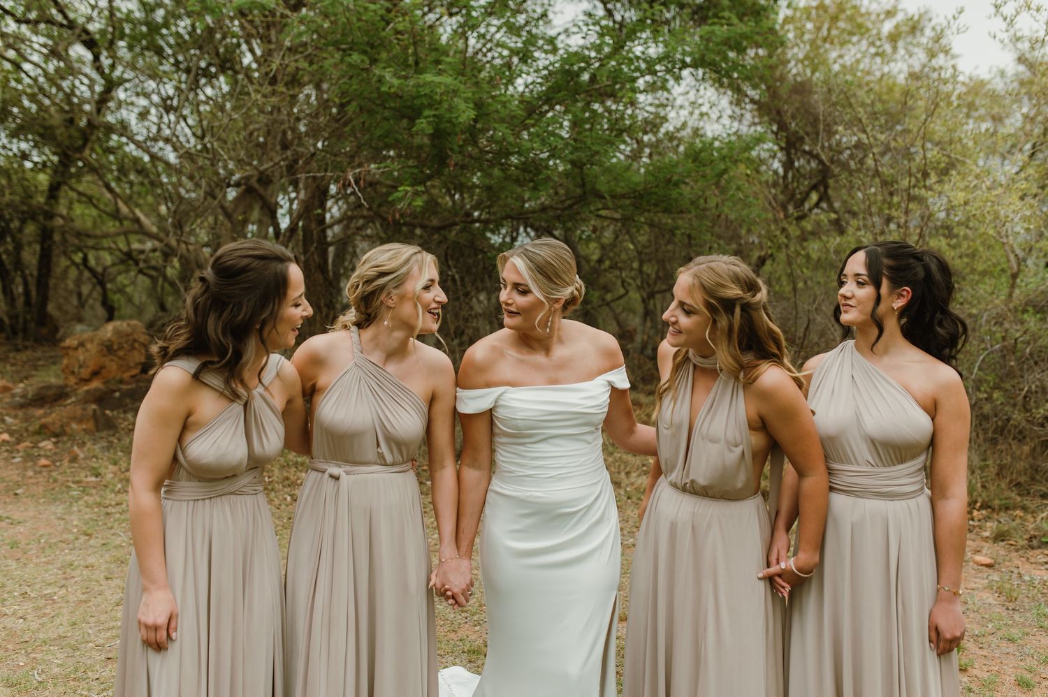 Wedding party in coordinated neutral dresses shares a candid moment outdoors.