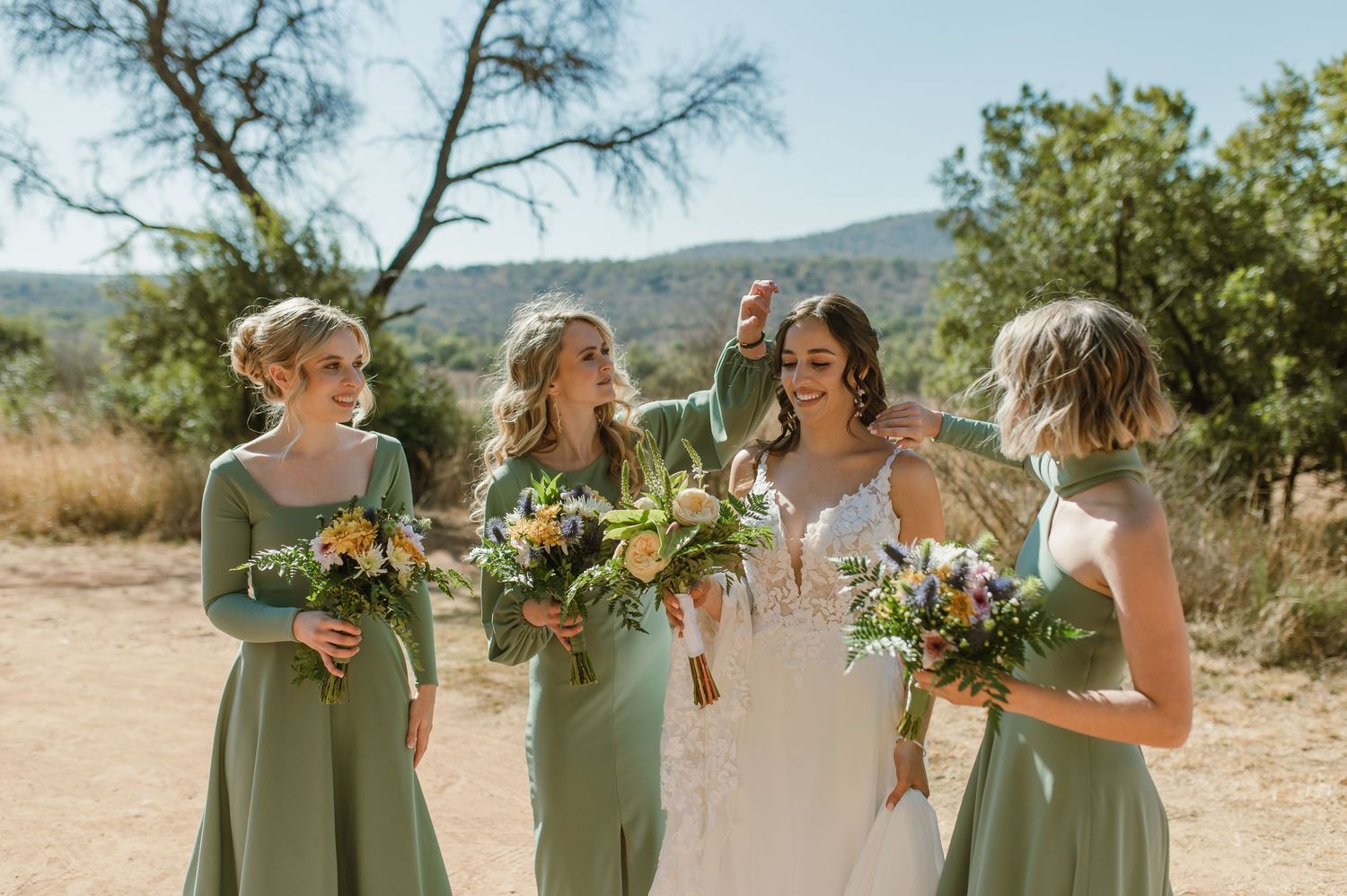 Wedding party lined up in sage green and white dresses against desert landscape.