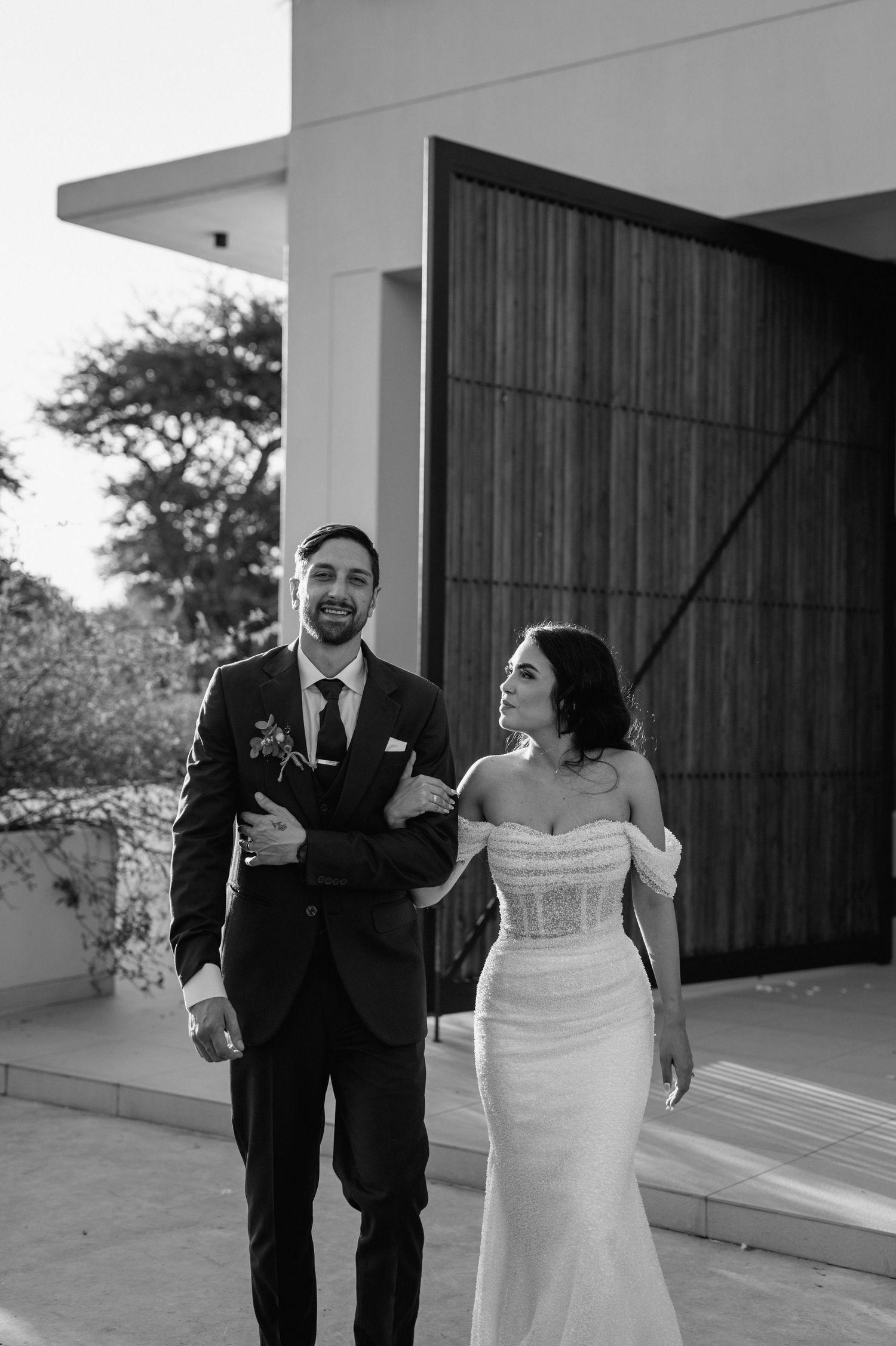 Playful wedding couple poses in black and white on modern patio.