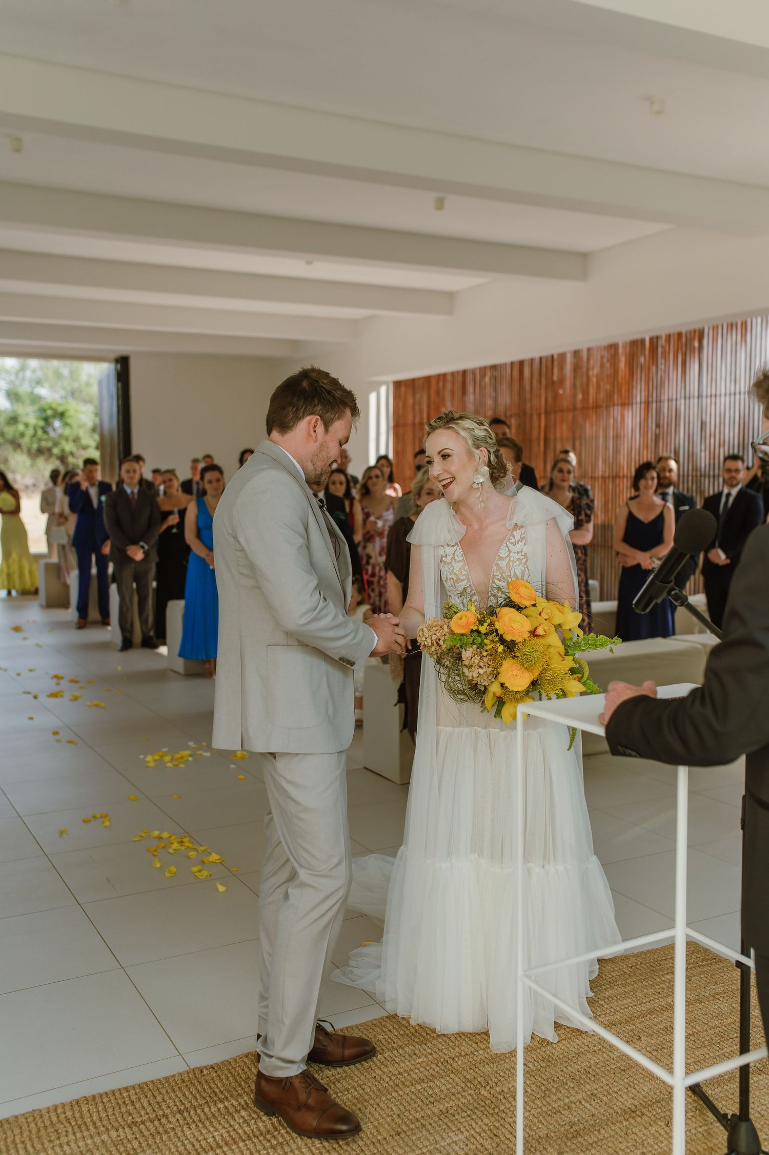 Wedding ceremony in a modern white room with guests watching a couple exchange vows.
