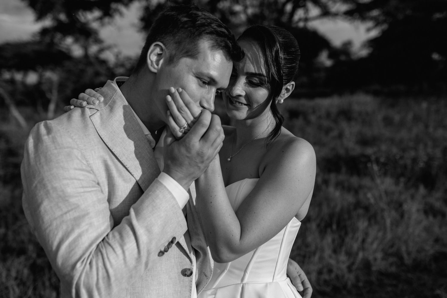An intimate black and white portrait of newlyweds sharing an emotional moment in a field.