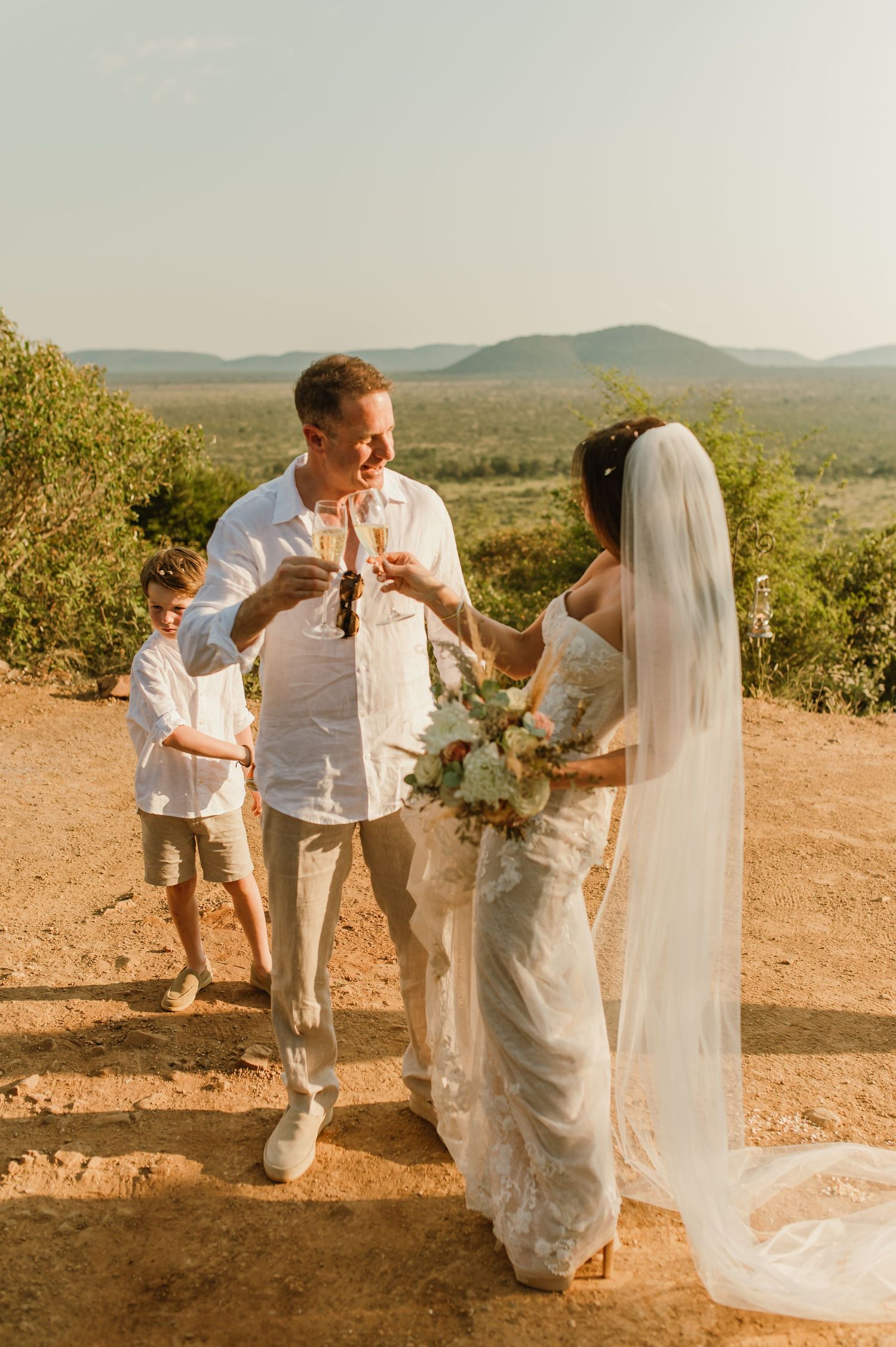 Bride and groom toasting with champagne at a scenic outdoor wedding with rolling hills in the background.