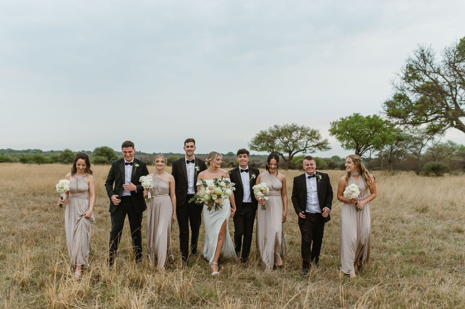 Wedding party poses informally across a scenic prairie landscape.