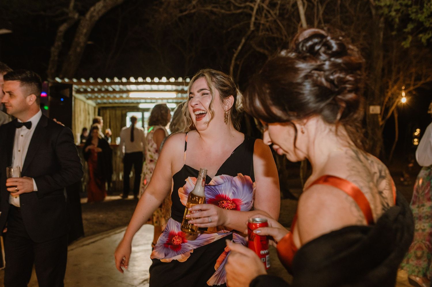 Wedding reception guests enjoying drinks and dancing in a rustic venue with string lights.