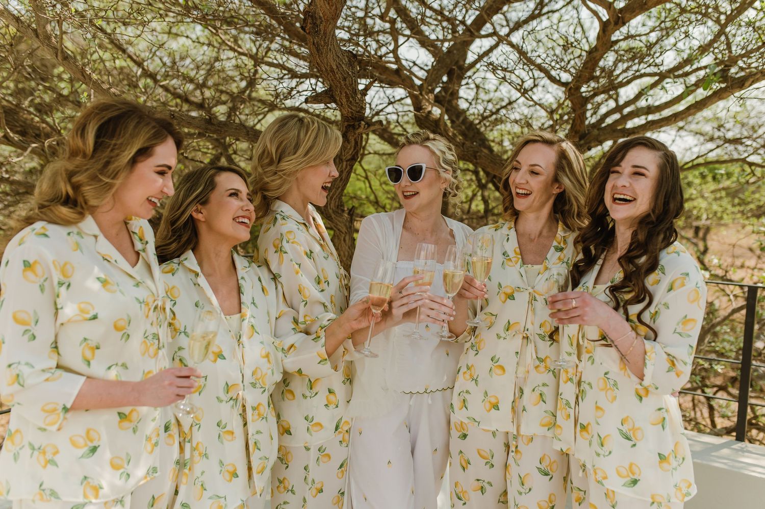 Wedding party in matching floral robes celebrating together under trees.