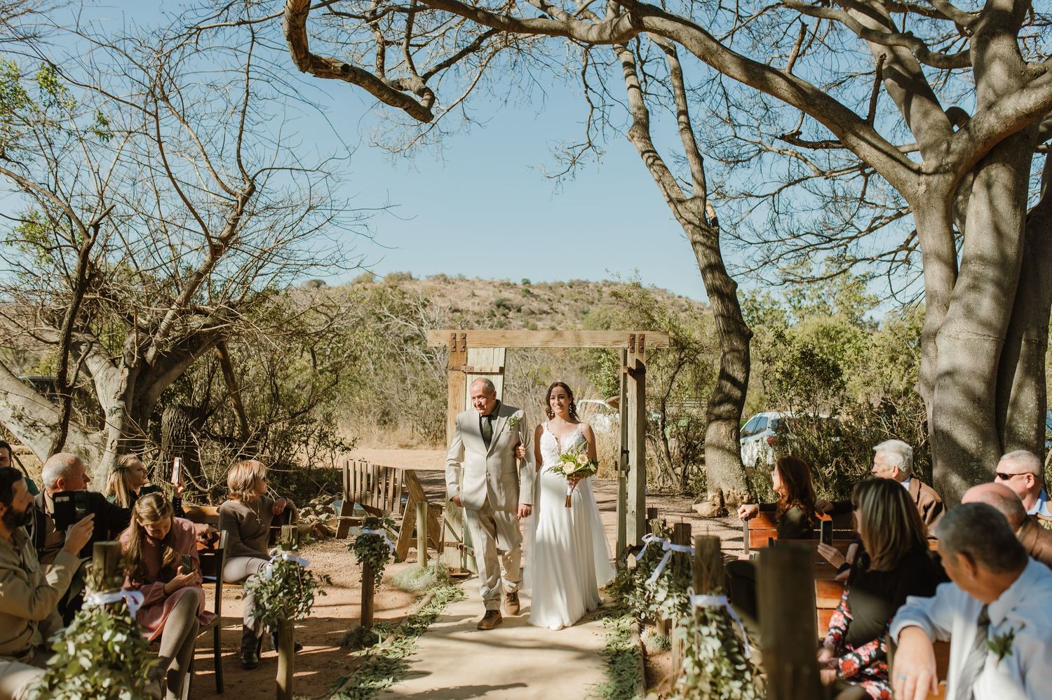 Wedding guests seated in wooden chairs during an outdoor desert ceremony.