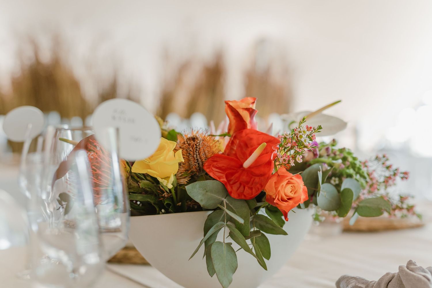 Close-up of wedding table centerpieces featuring coral and yellow flowers with greenery accents.