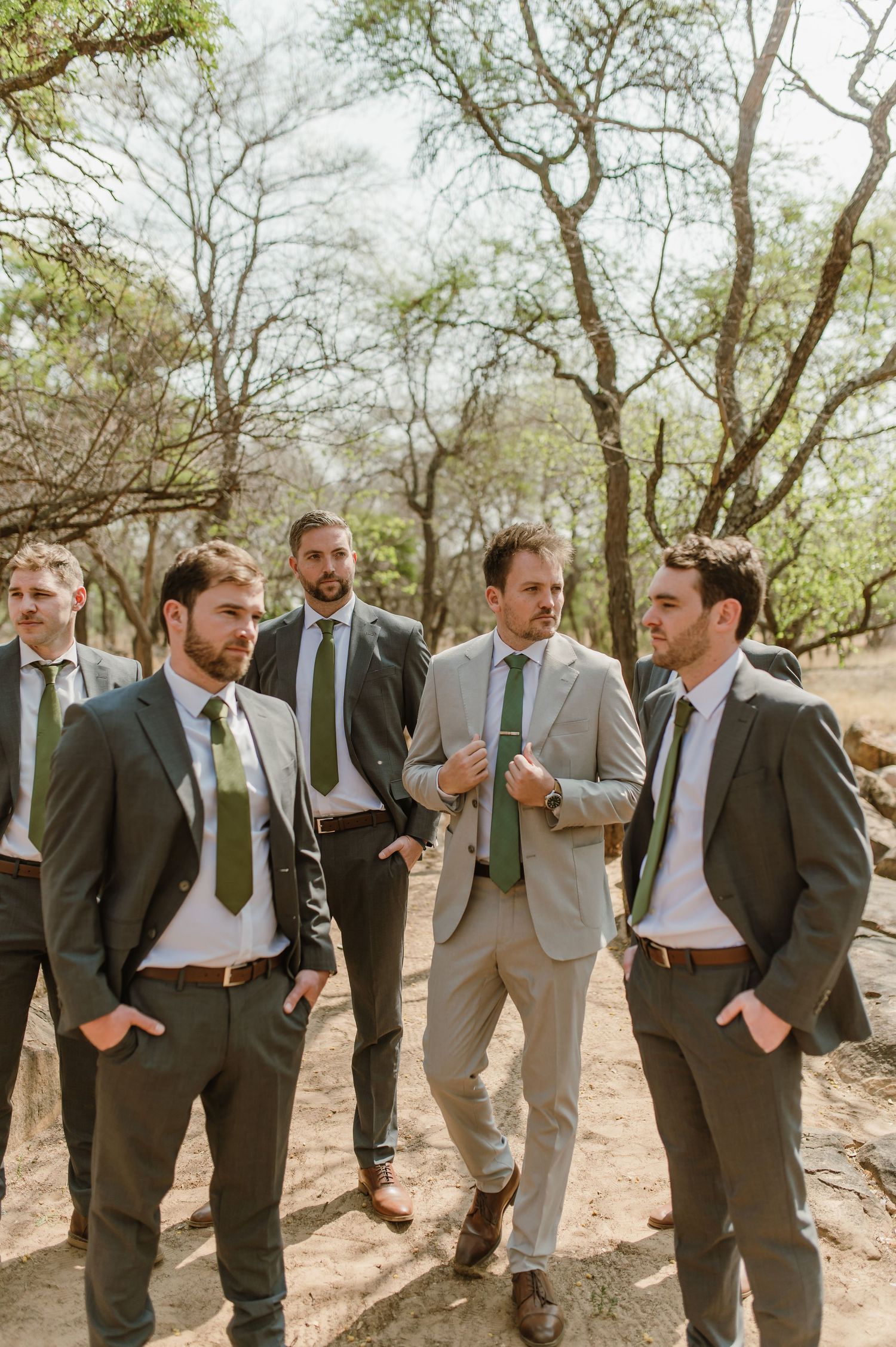 Wedding party in grey suits standing together in a wooded outdoor setting.