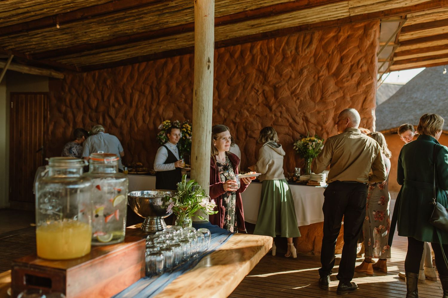 Rustic wedding reception venue with wooden beams and natural lighting showcases guests mingling during celebration.