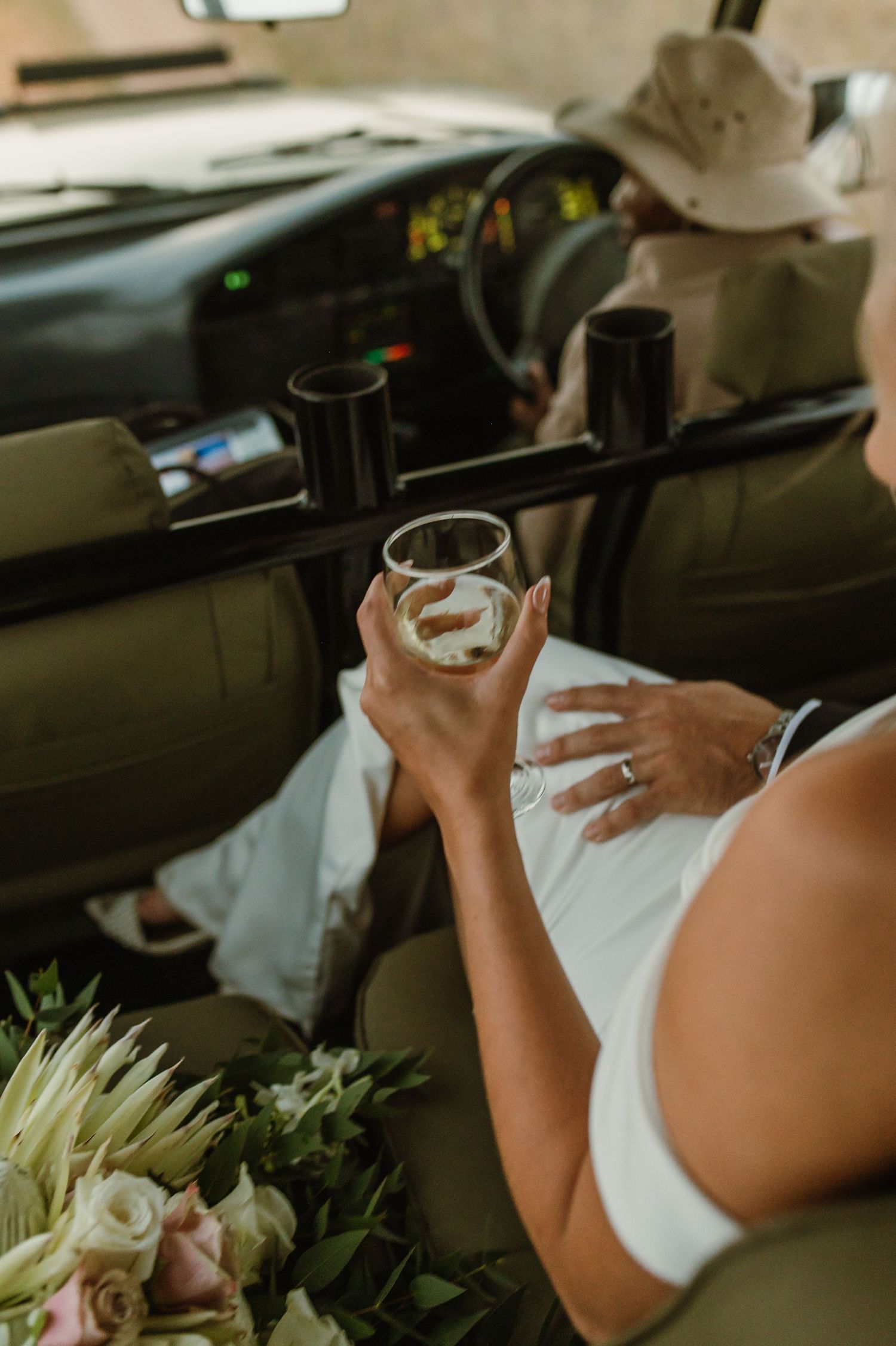 Wedding couple enjoying drinks together in safari vehicle during outdoor celebration.