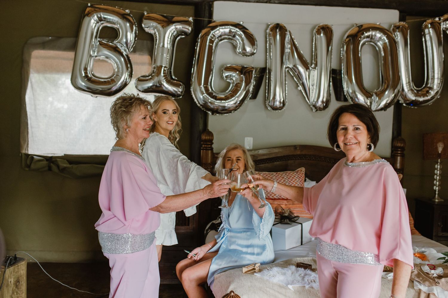 A bride and bridesmaids getting ready in a room with pink and blue robes.